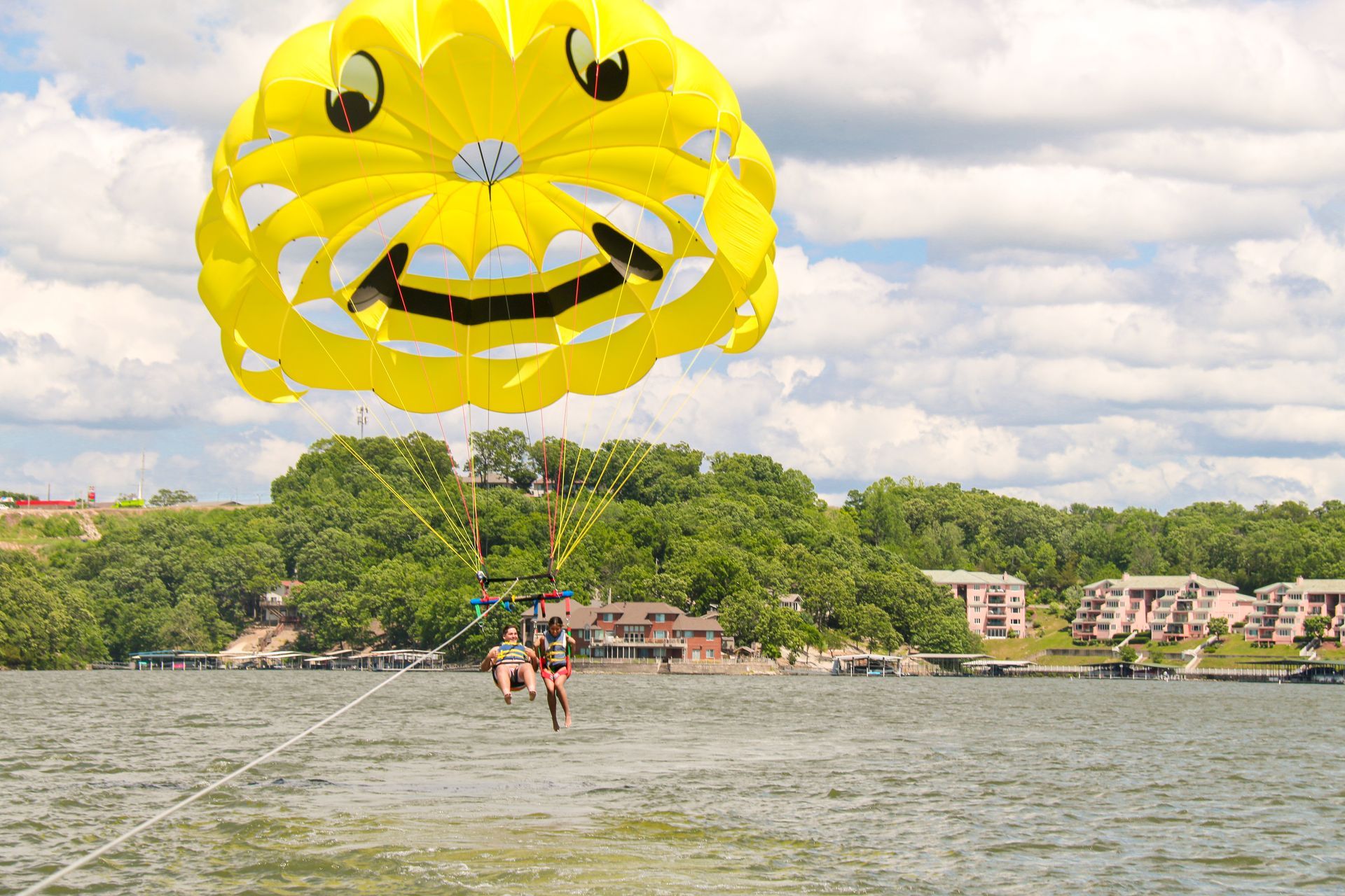 Yellow smiling parasail over a lake with people below and a shoreline in the background