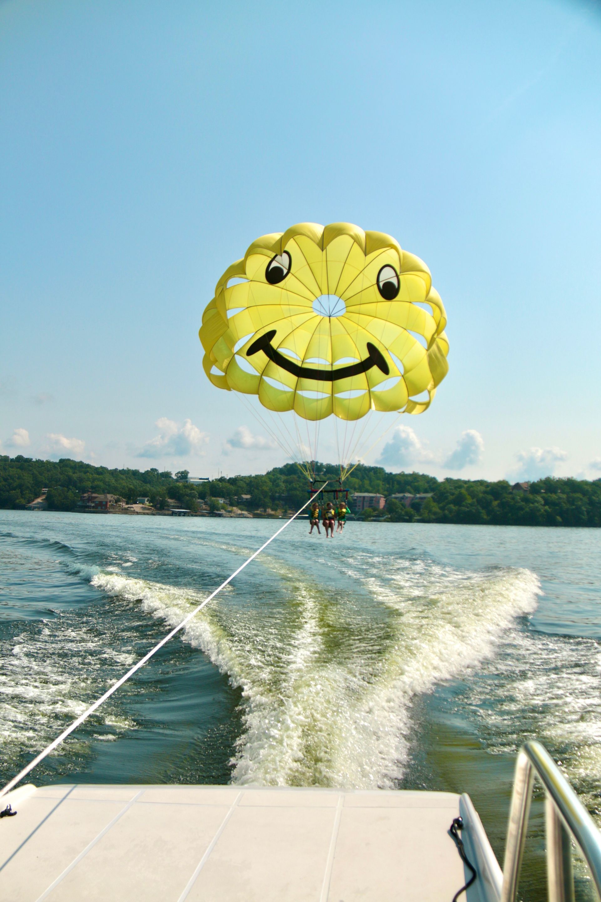 Yellow smiley-face parasail being towed over a lake behind a boat, with wake visible