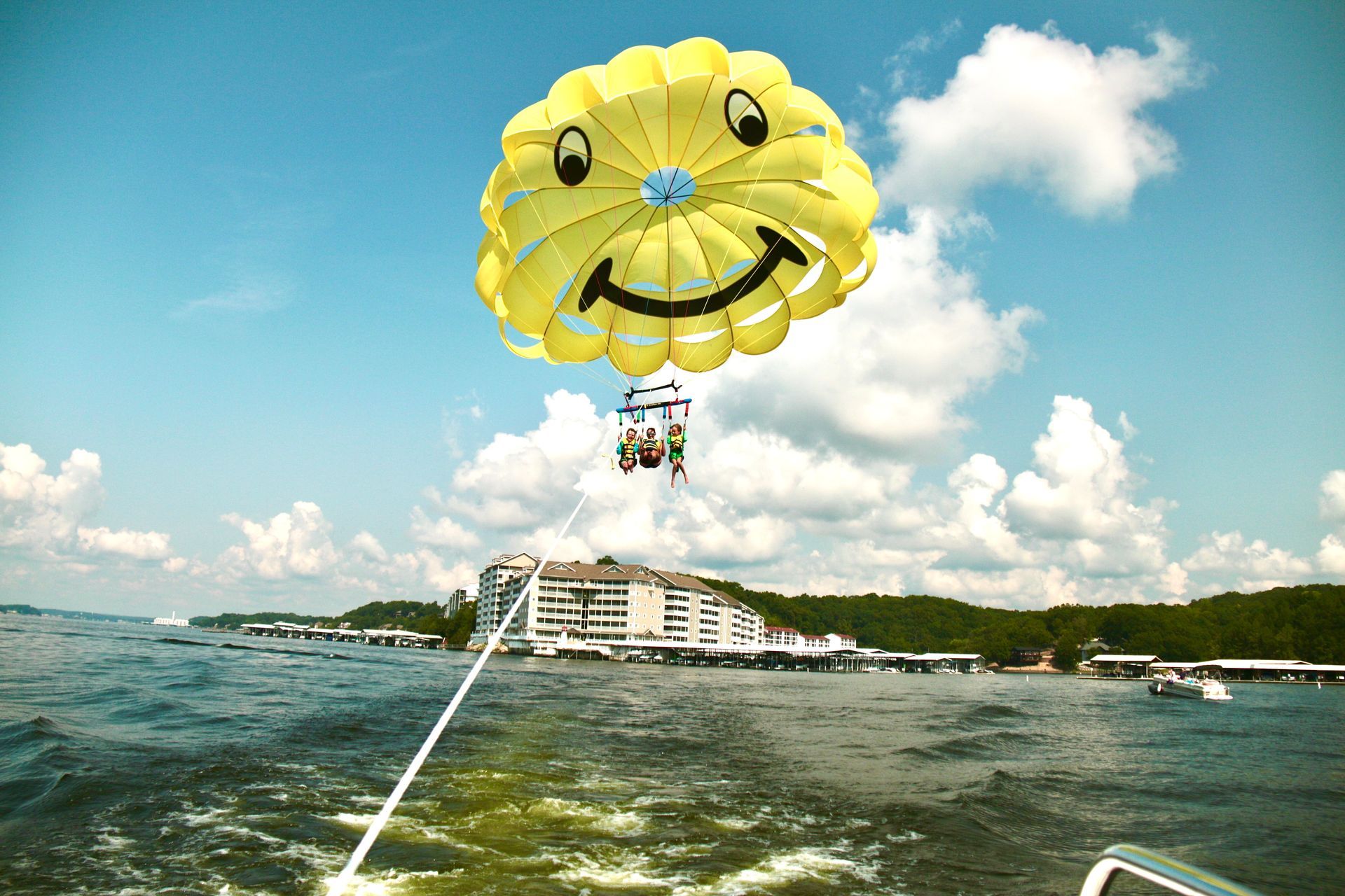 Yellow parasail over water near a resort, towing boat visible below and blue sky with clouds.