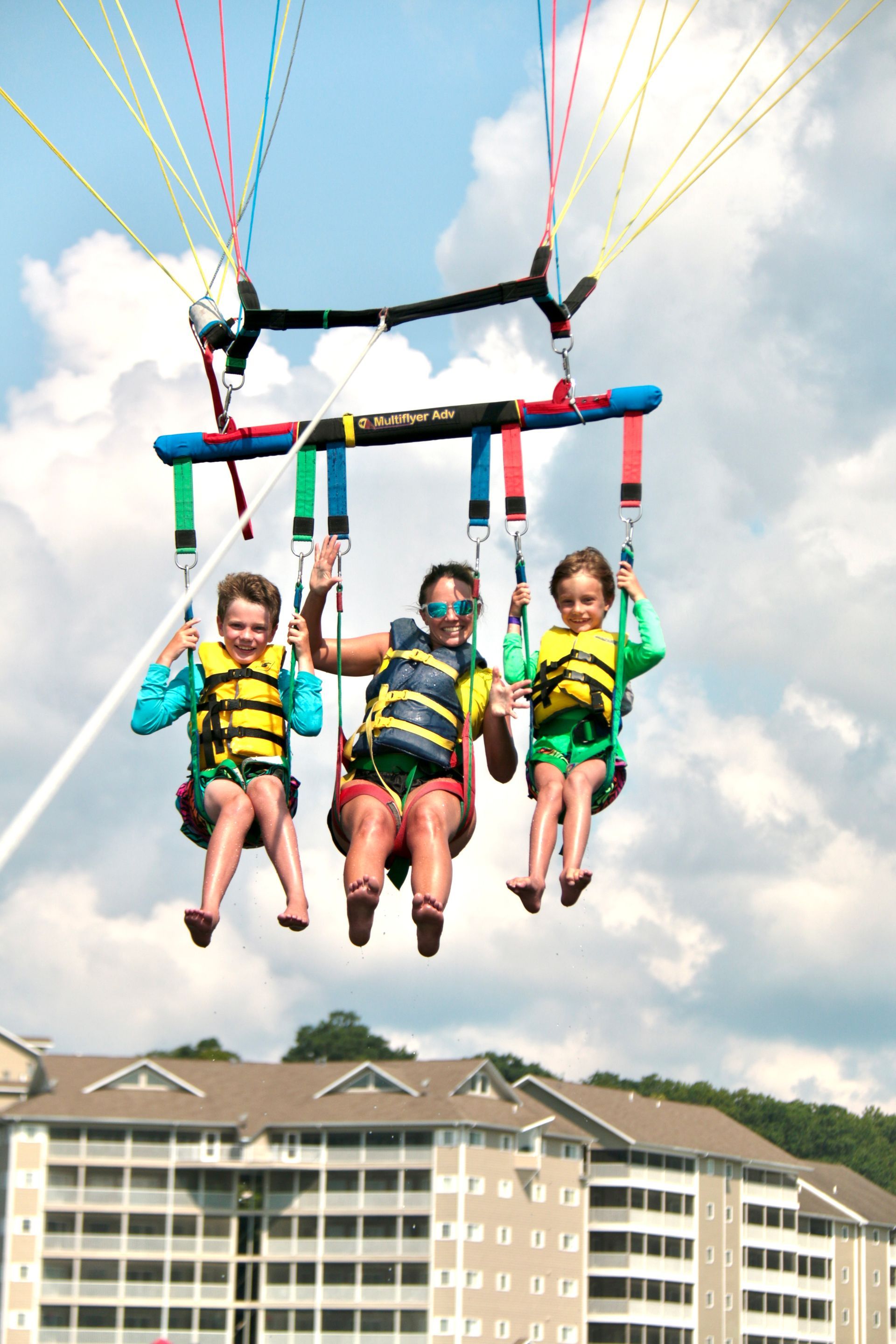 Three children parasailing in life jackets above a beach resort building