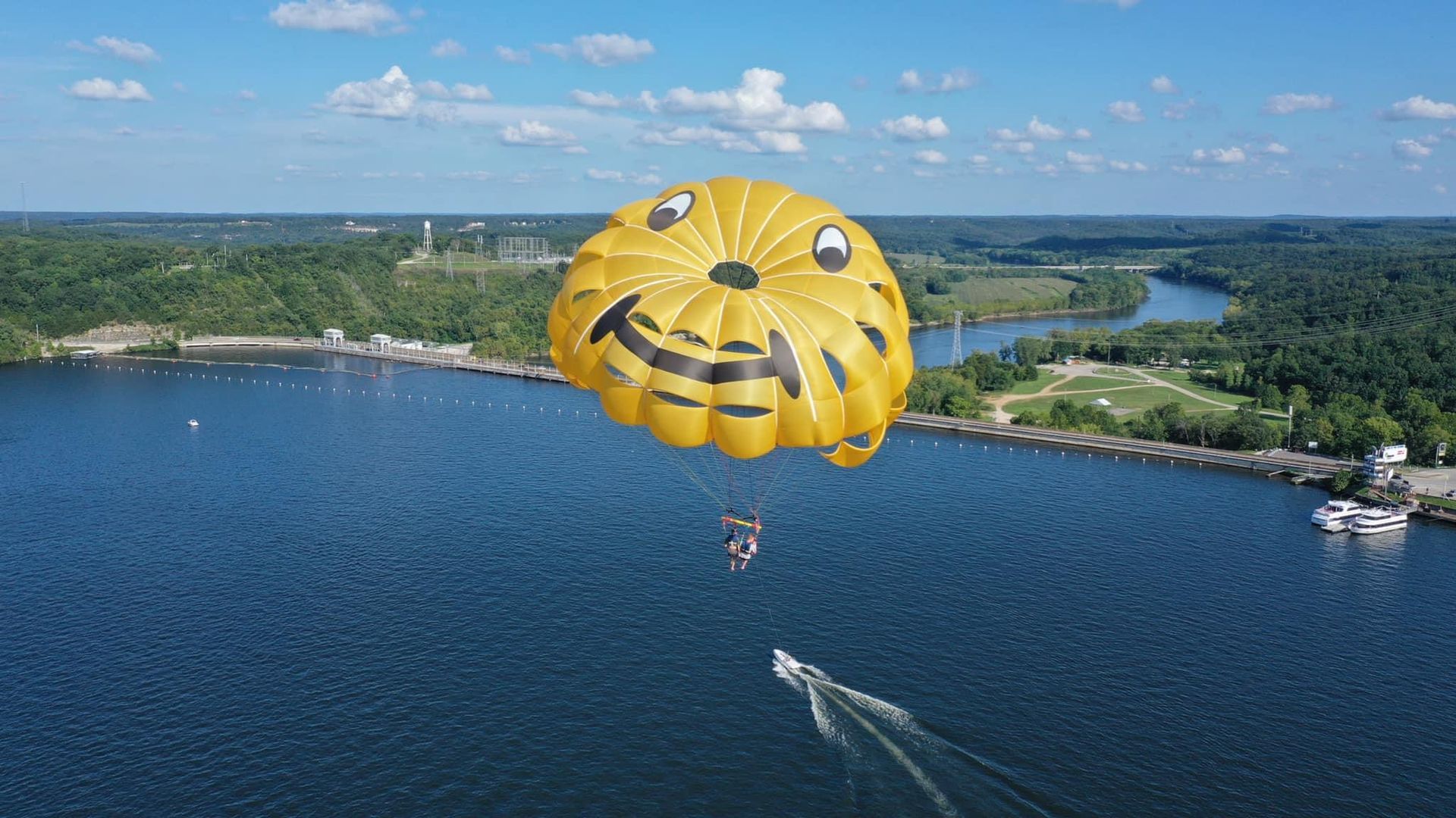 Yellow parachute above a blue lake with a boat below and green shoreline in the distance