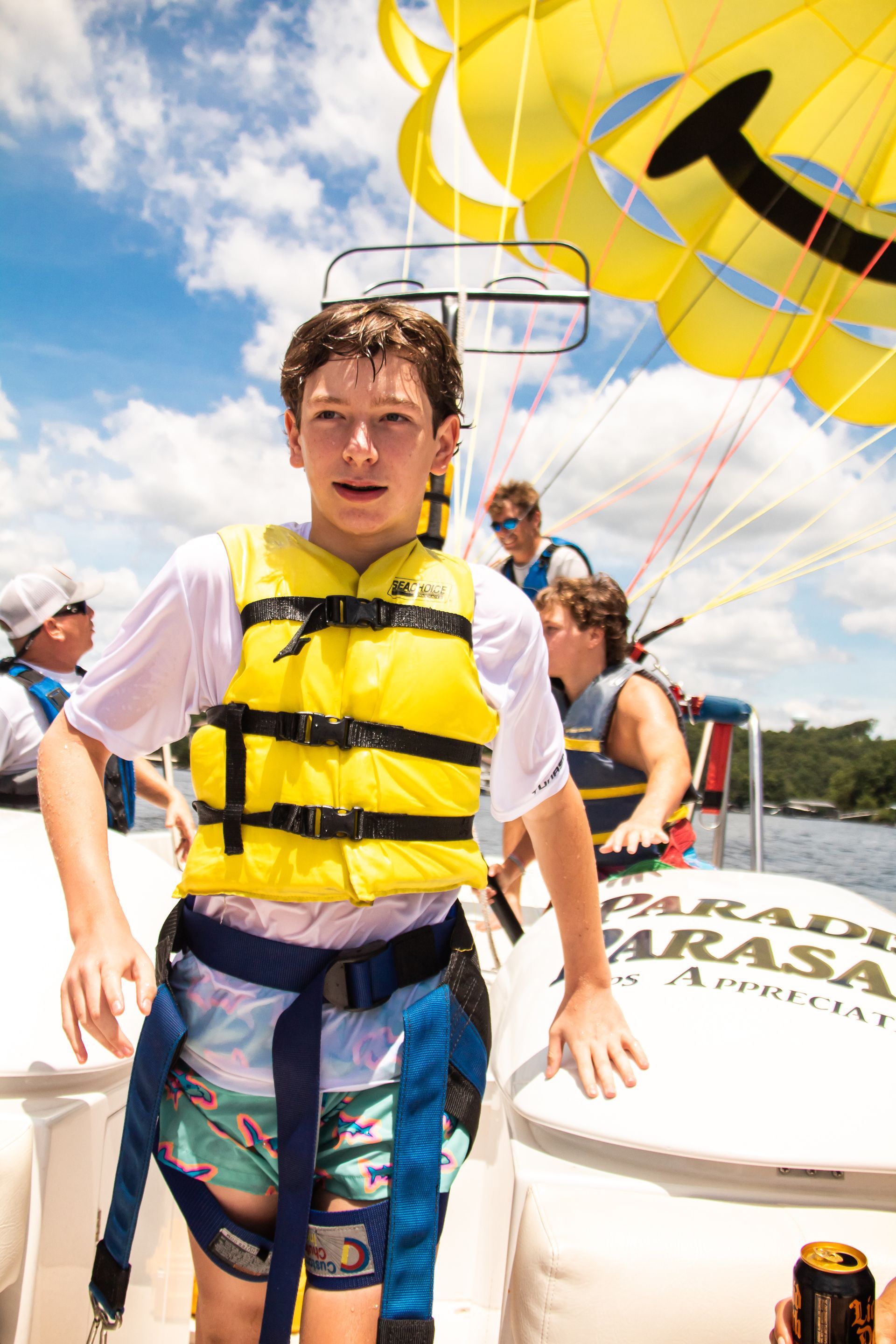 Person in a yellow life jacket parasailing on a boat, with a bright parachute overhead.