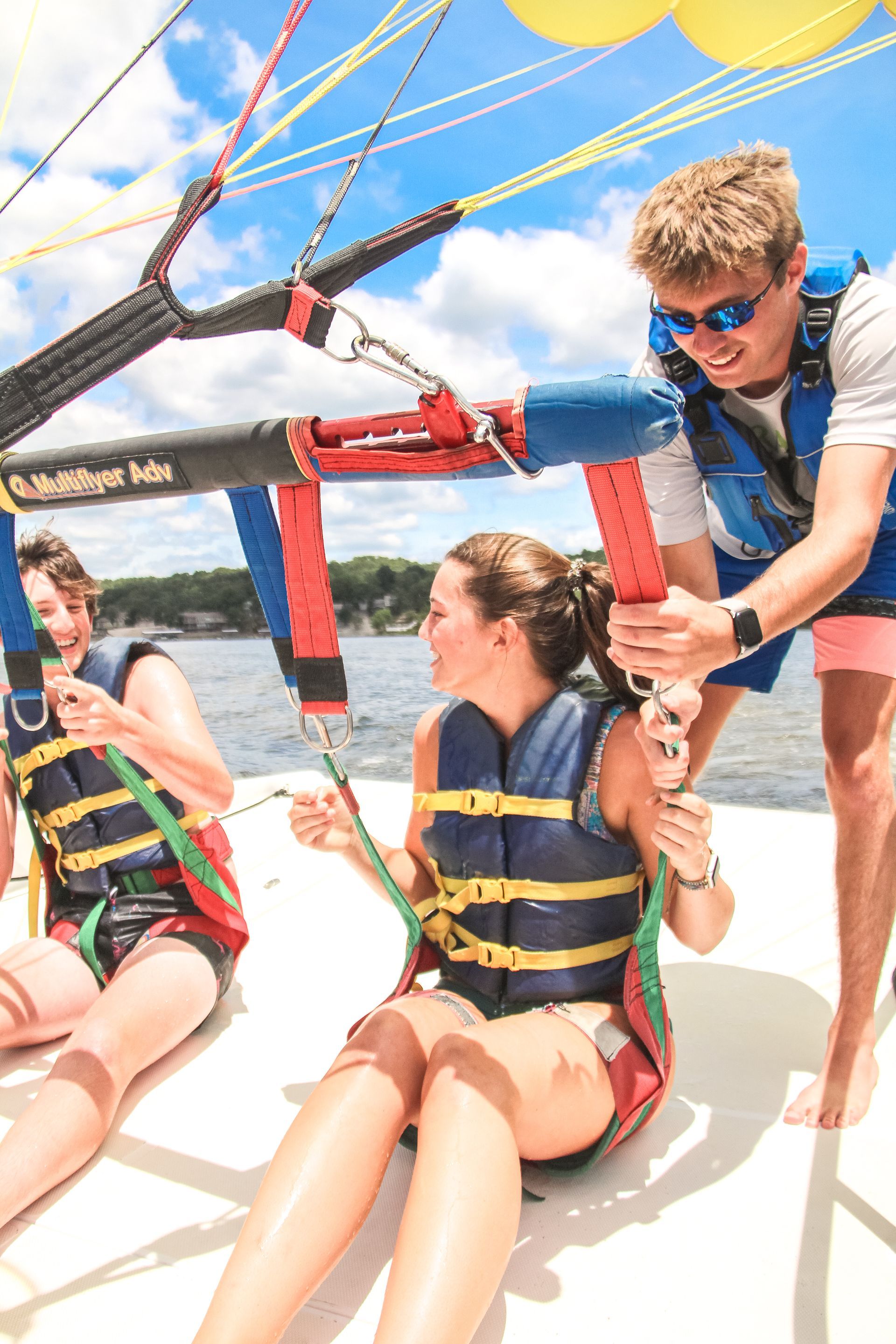 Two people parasailing in life jackets, seated on a boat under a bright blue sky.