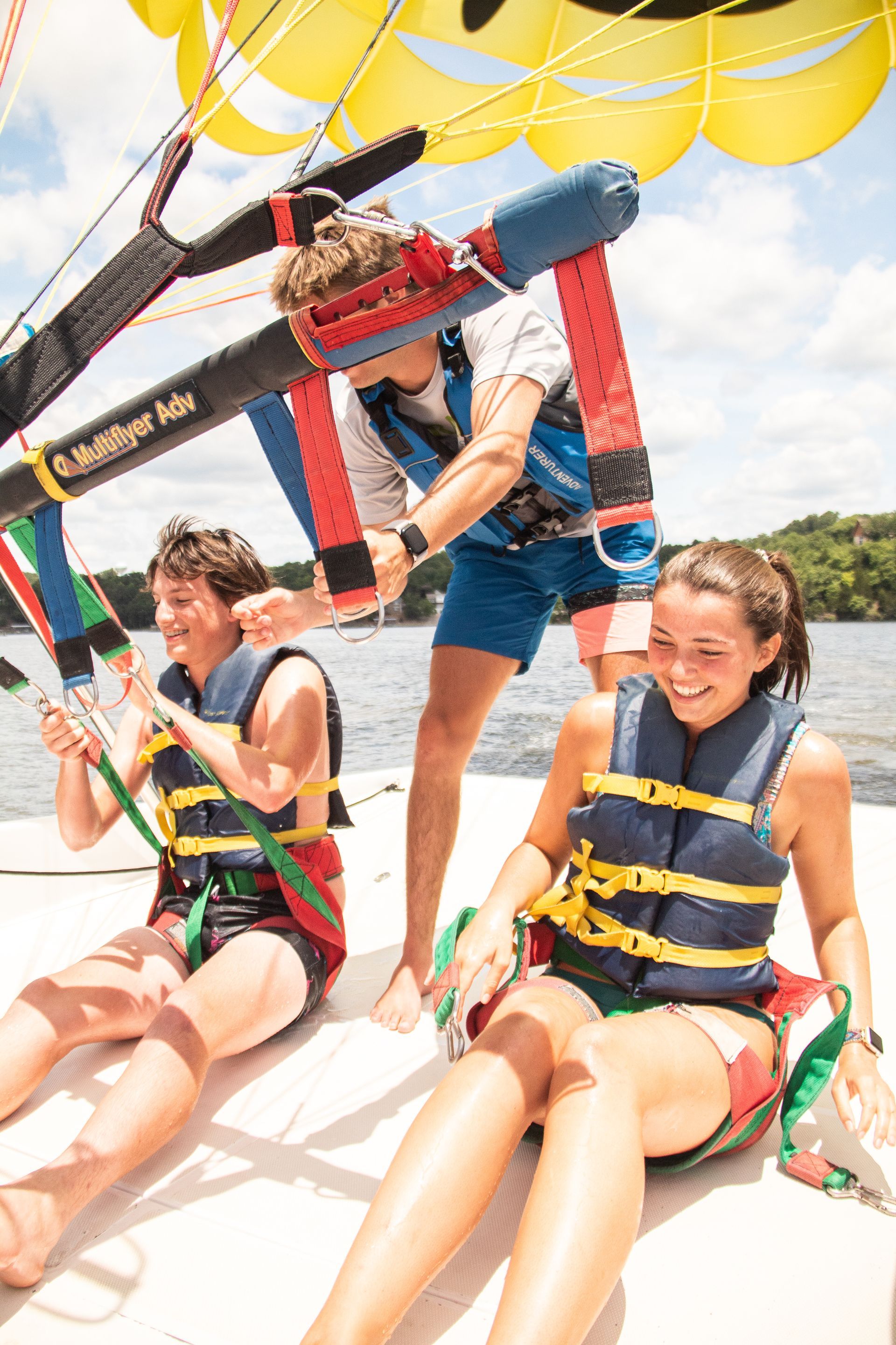 People parasailing over water, wearing life jackets and smiling under a yellow canopy