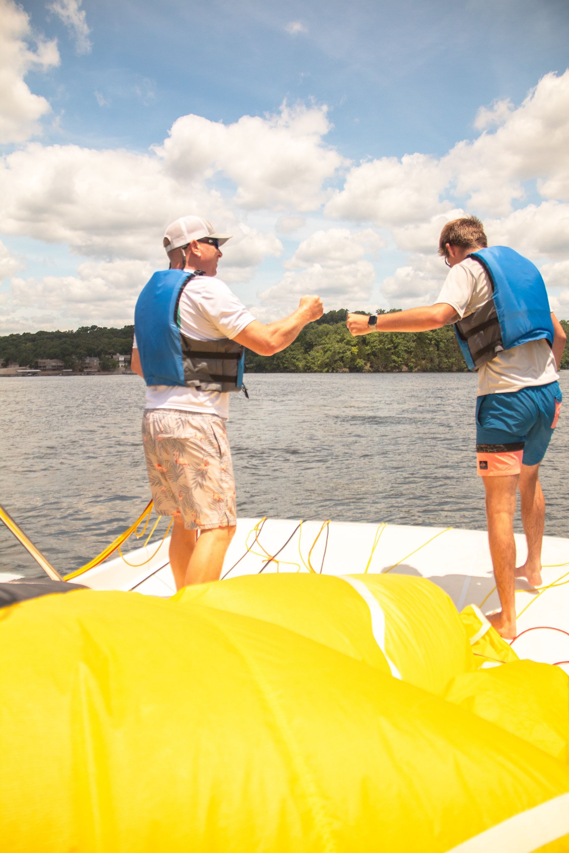 Two people in life vests stand on a yellow inflatable on a lake, facing each other and holding hands.
