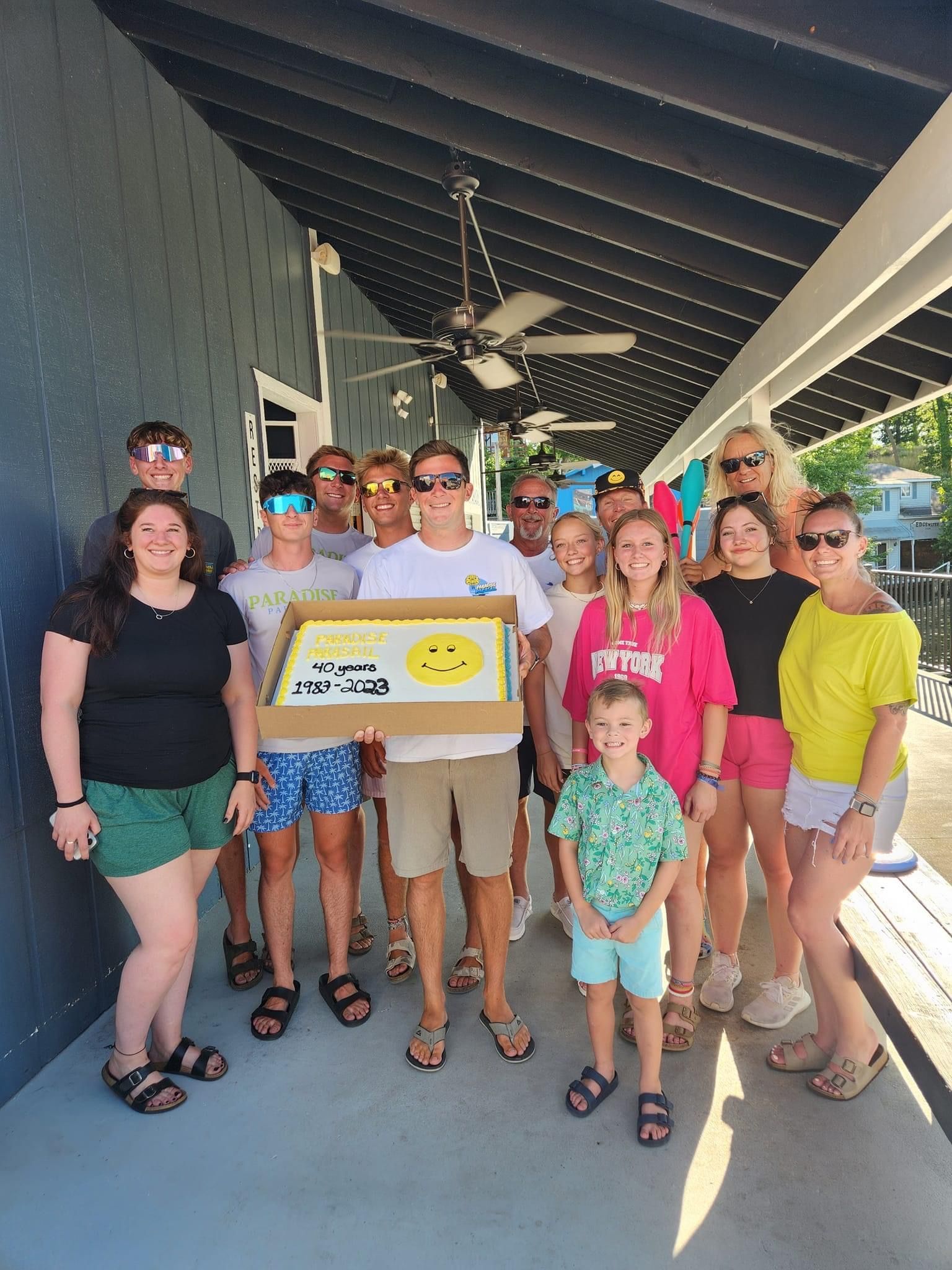 Group posing in a covered walkway, holding a large box with a smiley face and bright signs