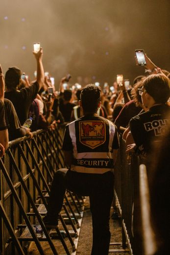Security guard watching a crowd holding up lit phones at a concert.