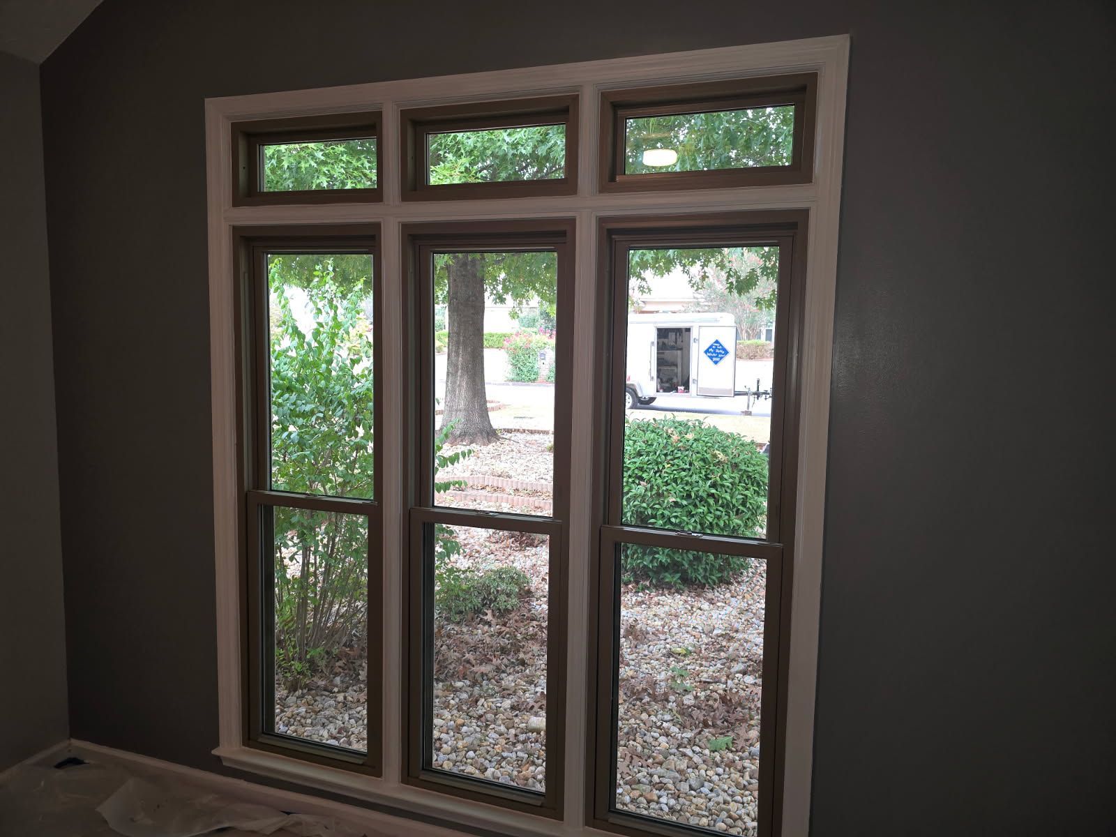 A room with three windows and a view of a yard.