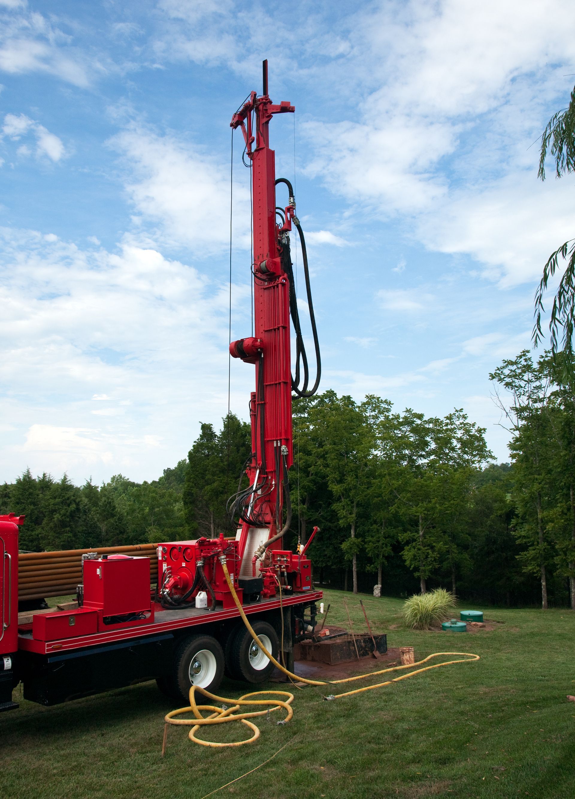 Red drilling rig on a truck in a grassy field under a cloudy sky
