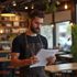 Man in apron, reviewing papers inside a cafe.