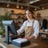 Woman wearing apron smiles at a cash register in a store.