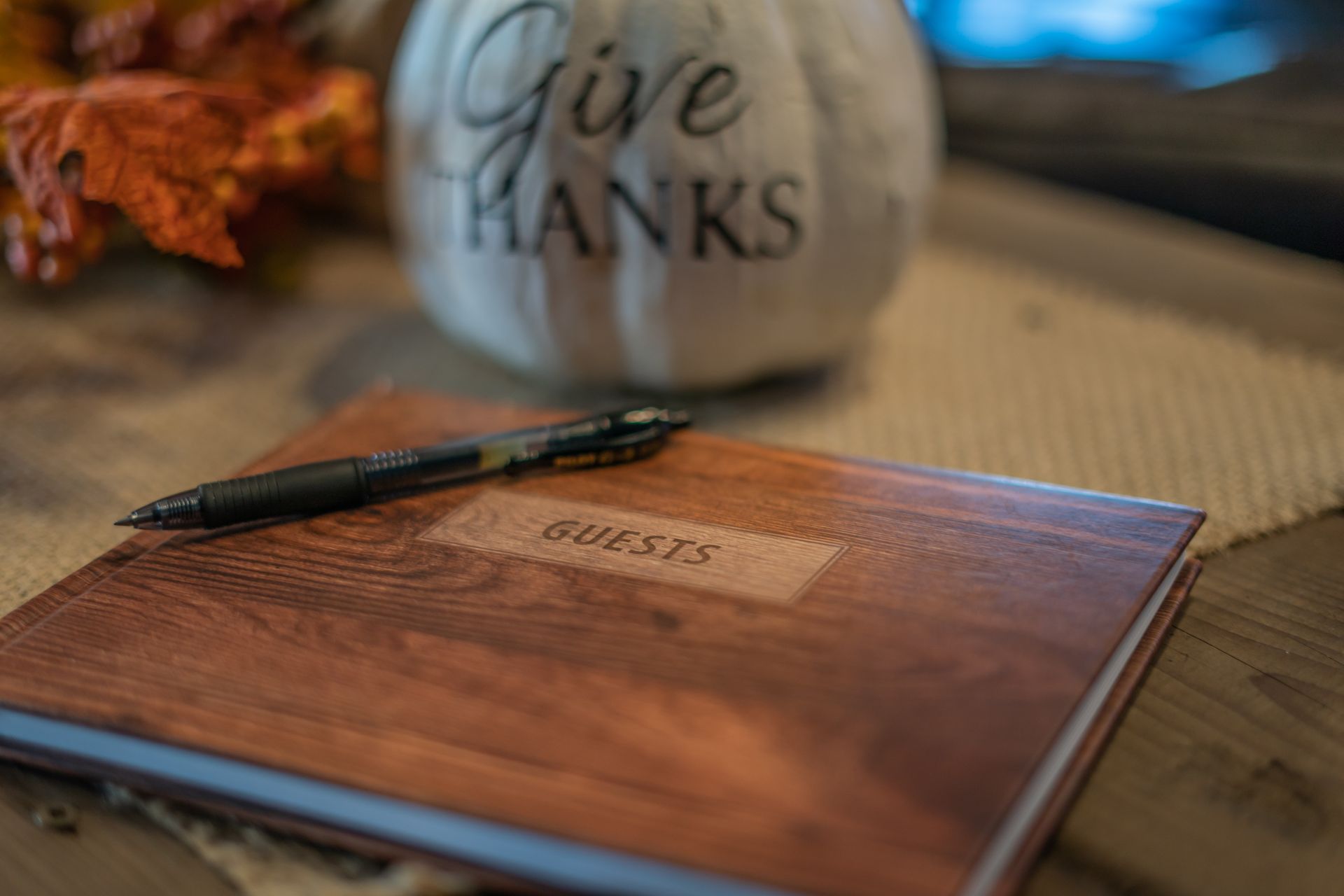 A wooden guest book with a pen on it is sitting on a table next to a pumpkin.