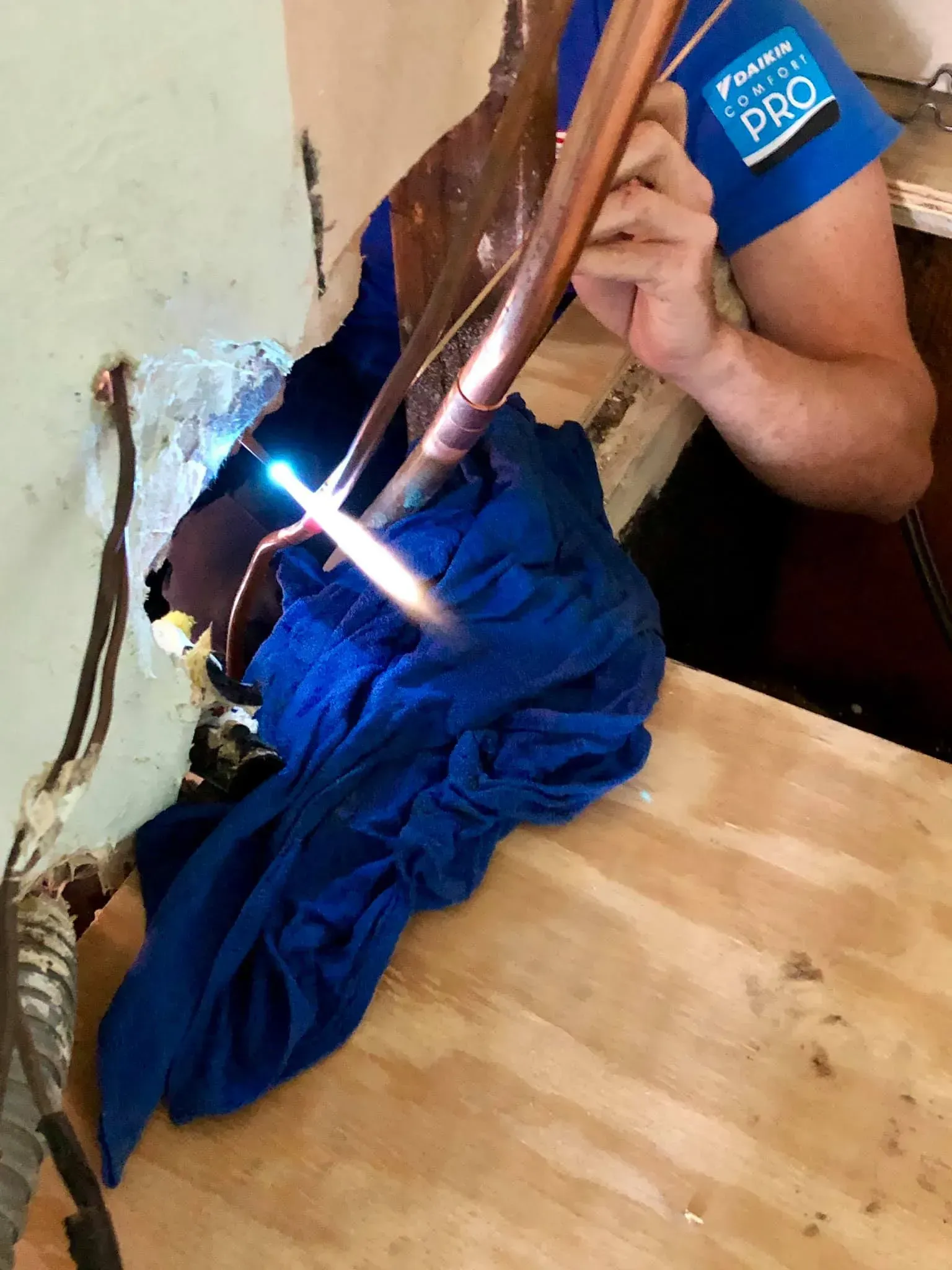 A person is welding copper pipes on a wooden table.