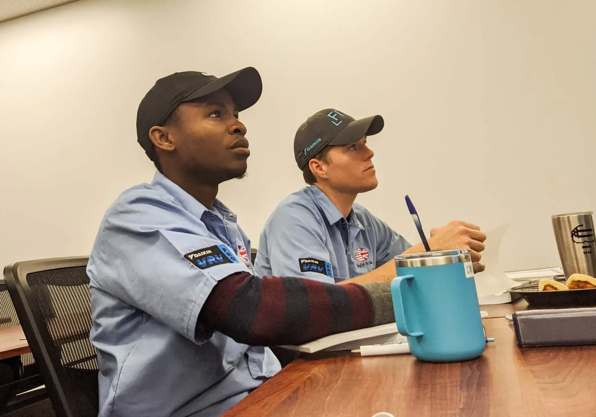 Two men are sitting at a table with a blue mug on it.