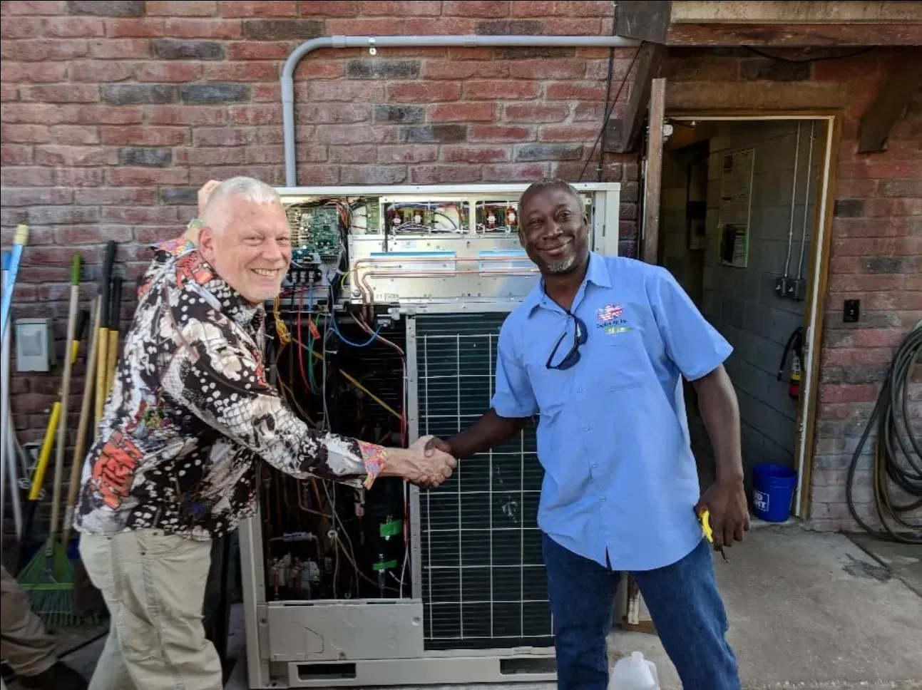 Two men are shaking hands in front of a broken air conditioner.