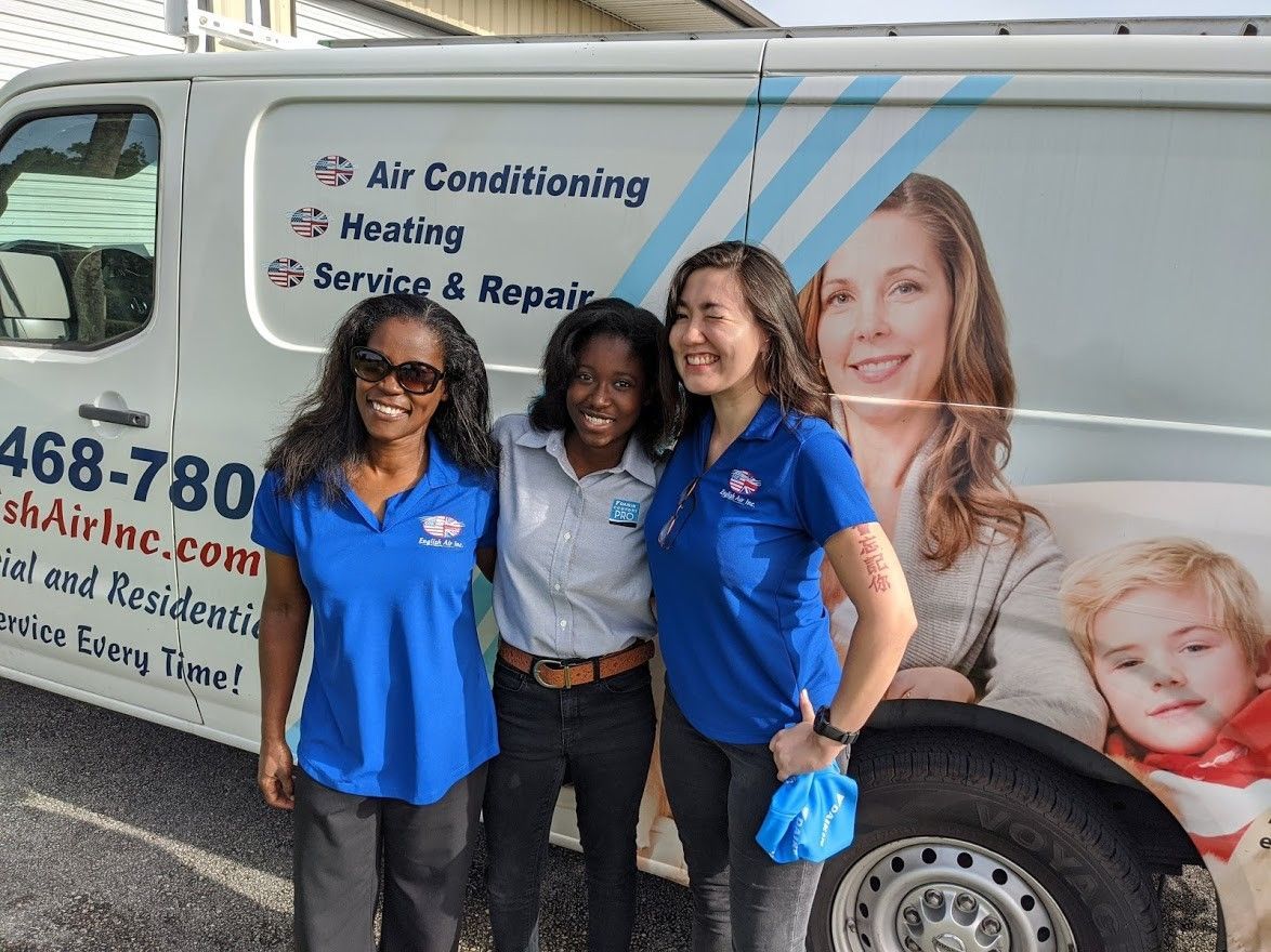Three women are posing for a picture in front of an air conditioning van.