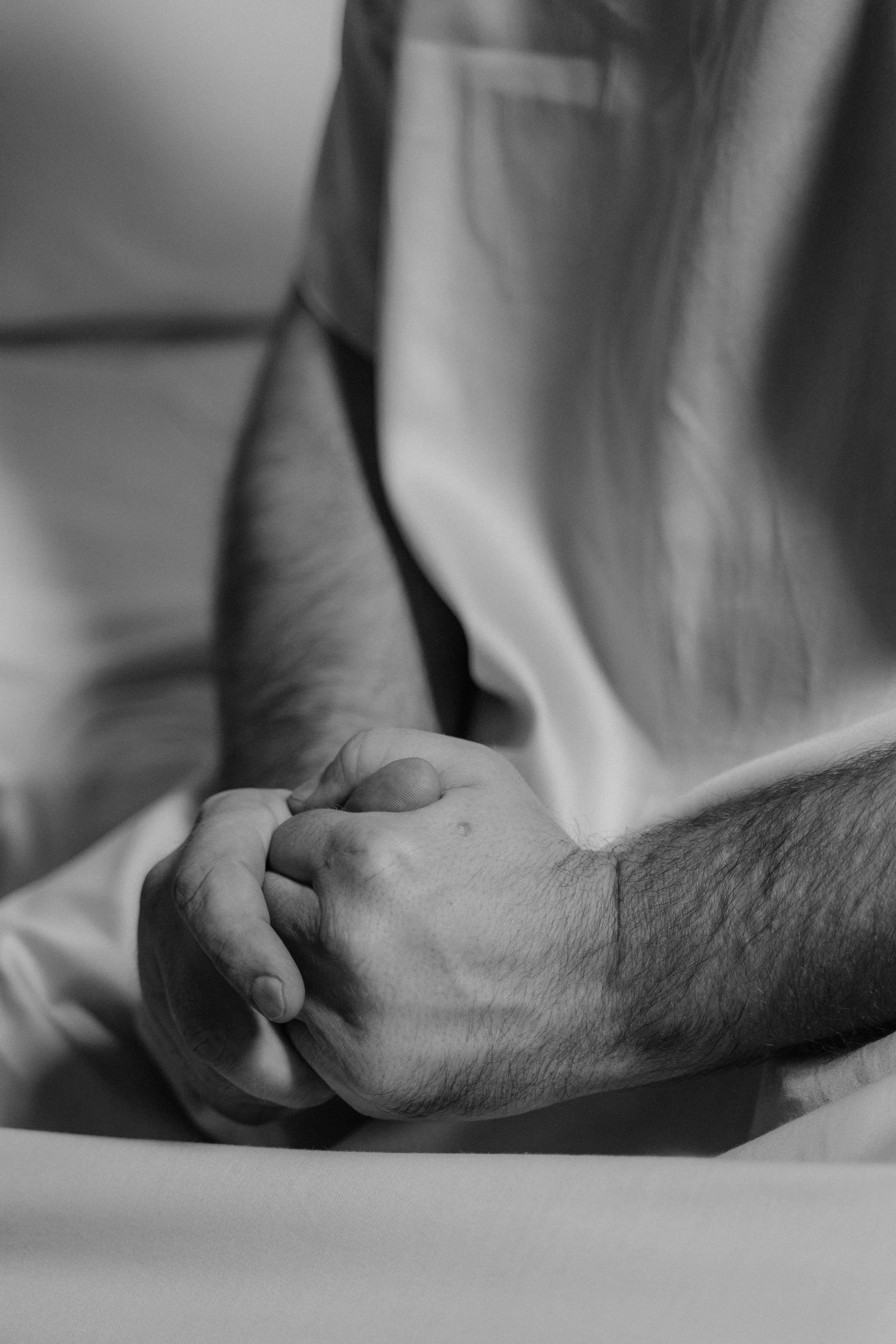 Man's clasped hands resting on a white surface, suggesting prayer or contemplation. Black and white.