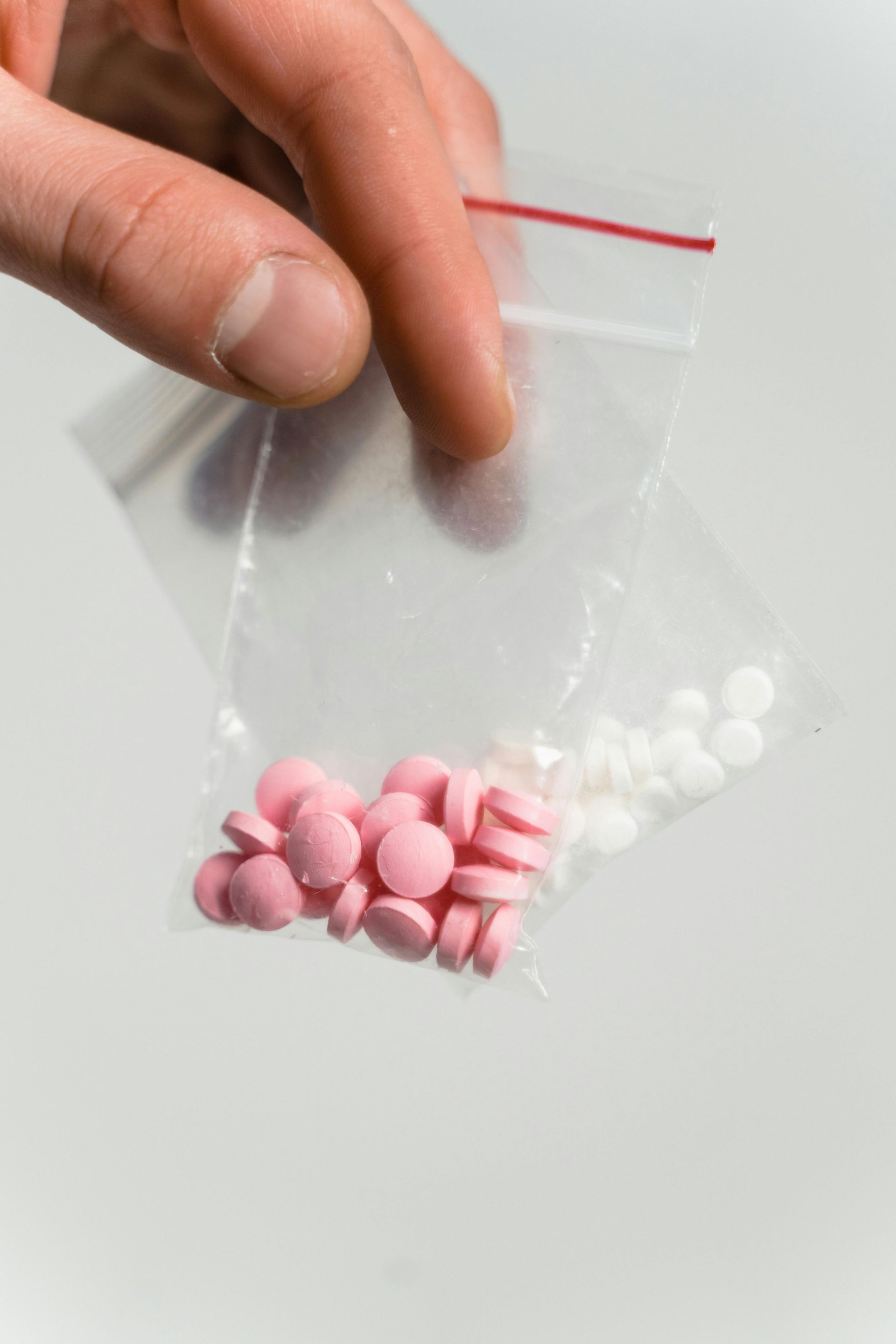 Hand holding a clear plastic bag with pink and white pills inside.
