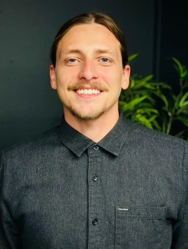 Man with long hair smiling, wearing a dark button-up shirt.