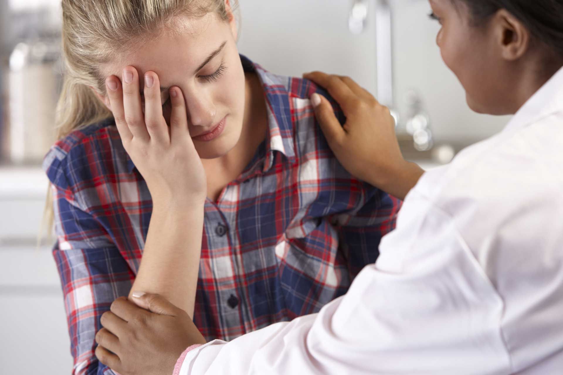 Woman with hand on her face, comforted by person in white coat.