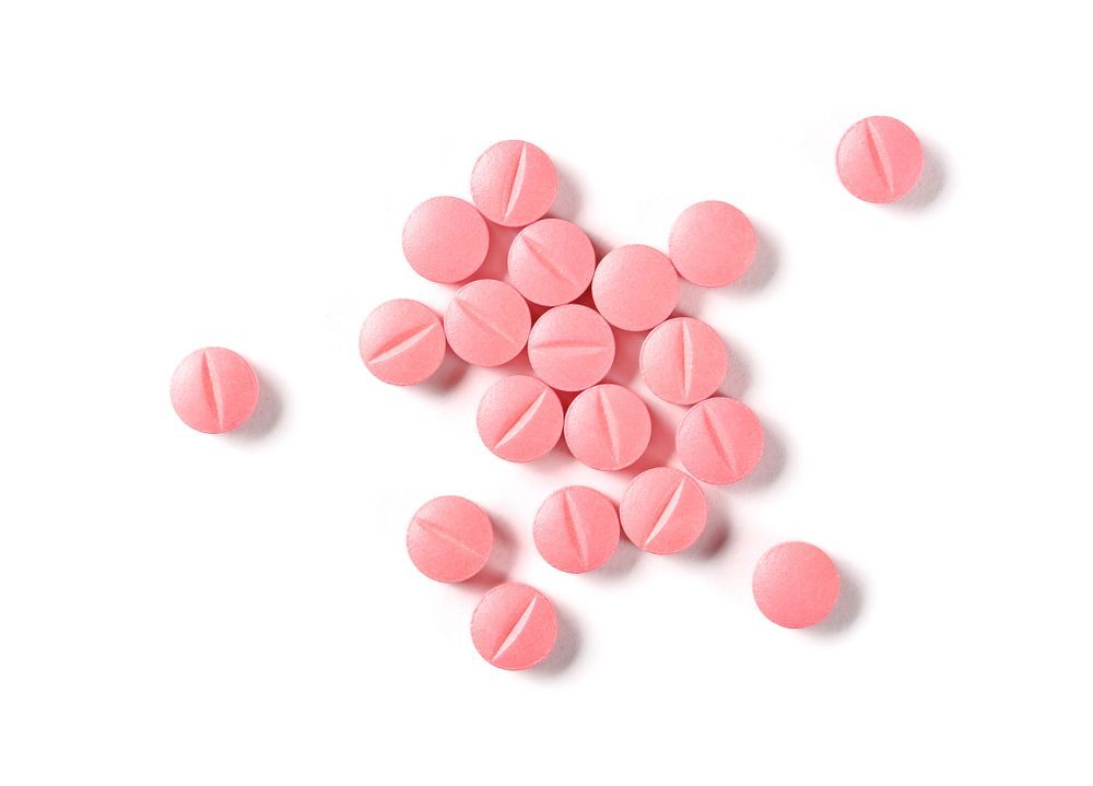 Pink pills scattered on a white surface, each with a central score line.