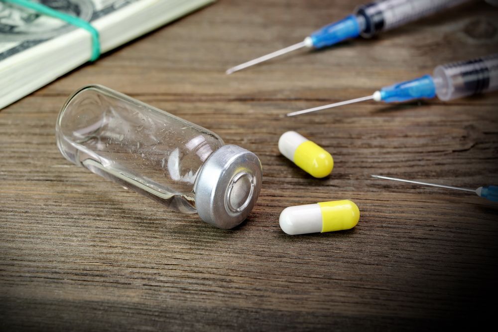 Money, syringes, a vial, and pills on a wooden surface.