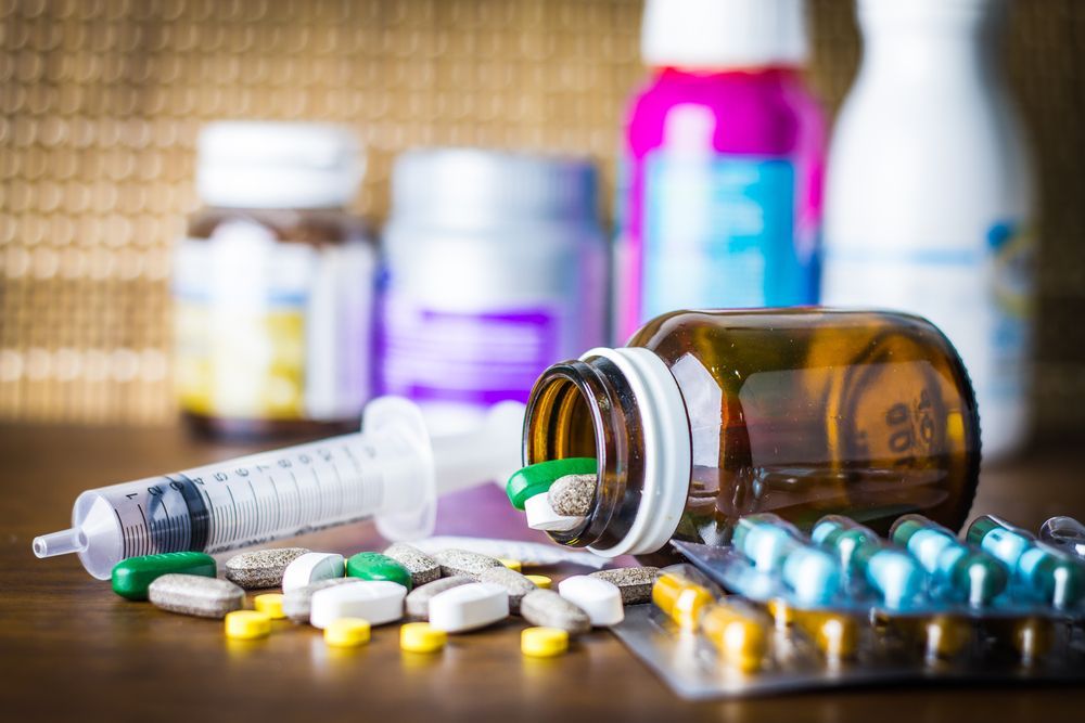 Pills spilling from a bottle, syringe, and medicine bottles on a wooden surface.