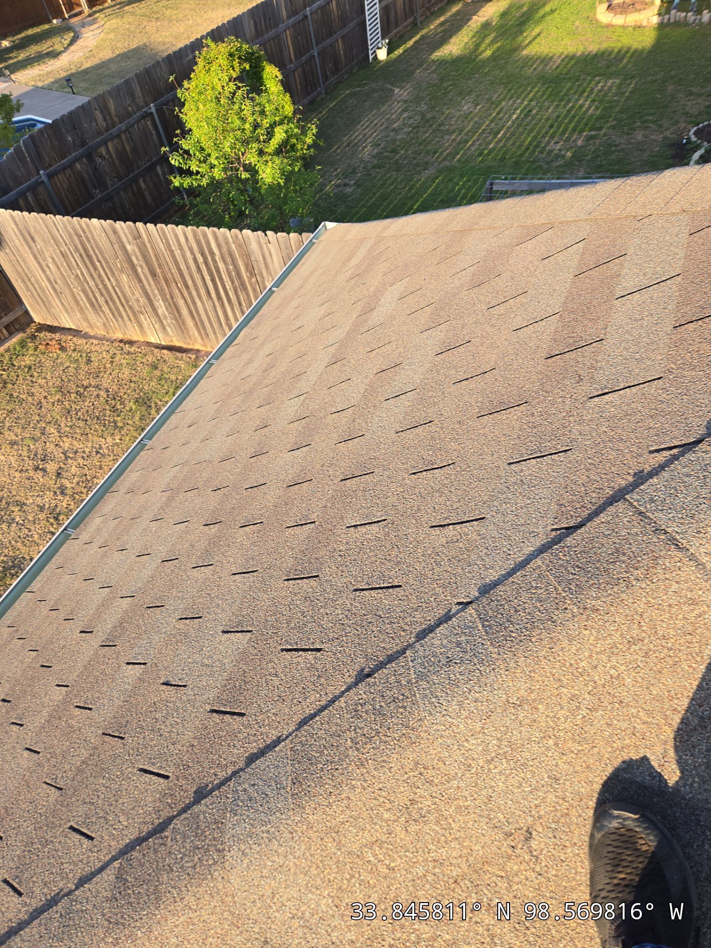 A person is standing on top of a roof with a fence in the background.