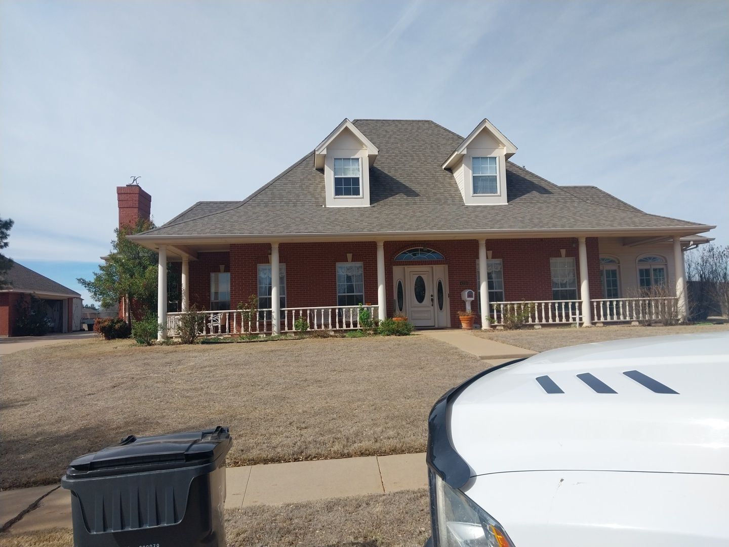 A white truck is parked in front of a large brick house