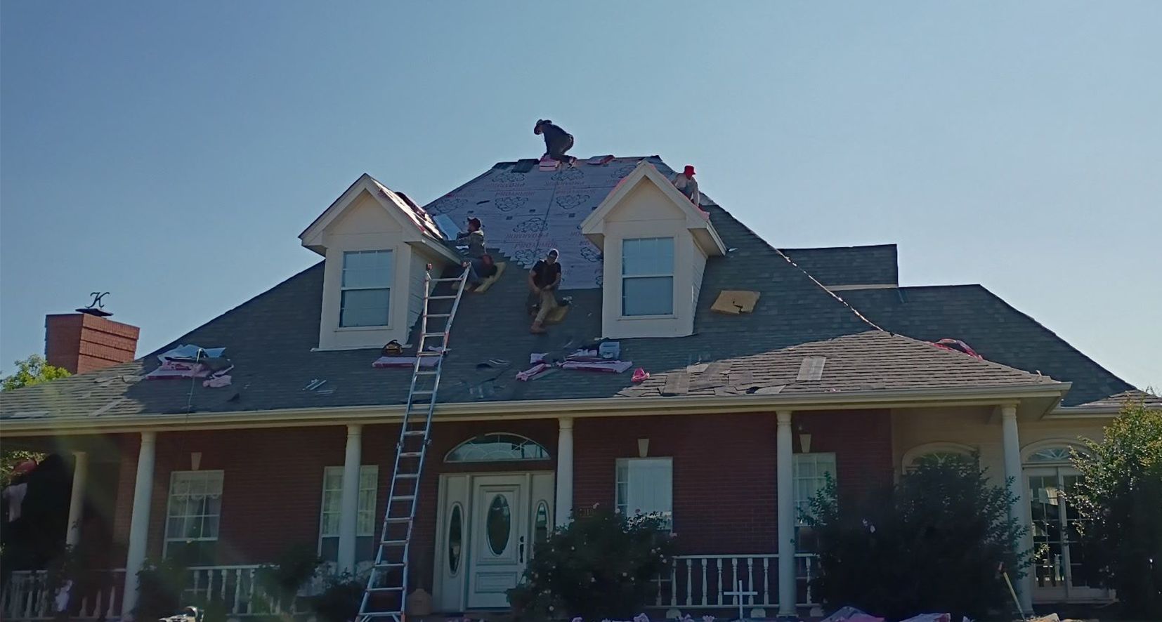 A man is standing on a ladder on the roof of a house.