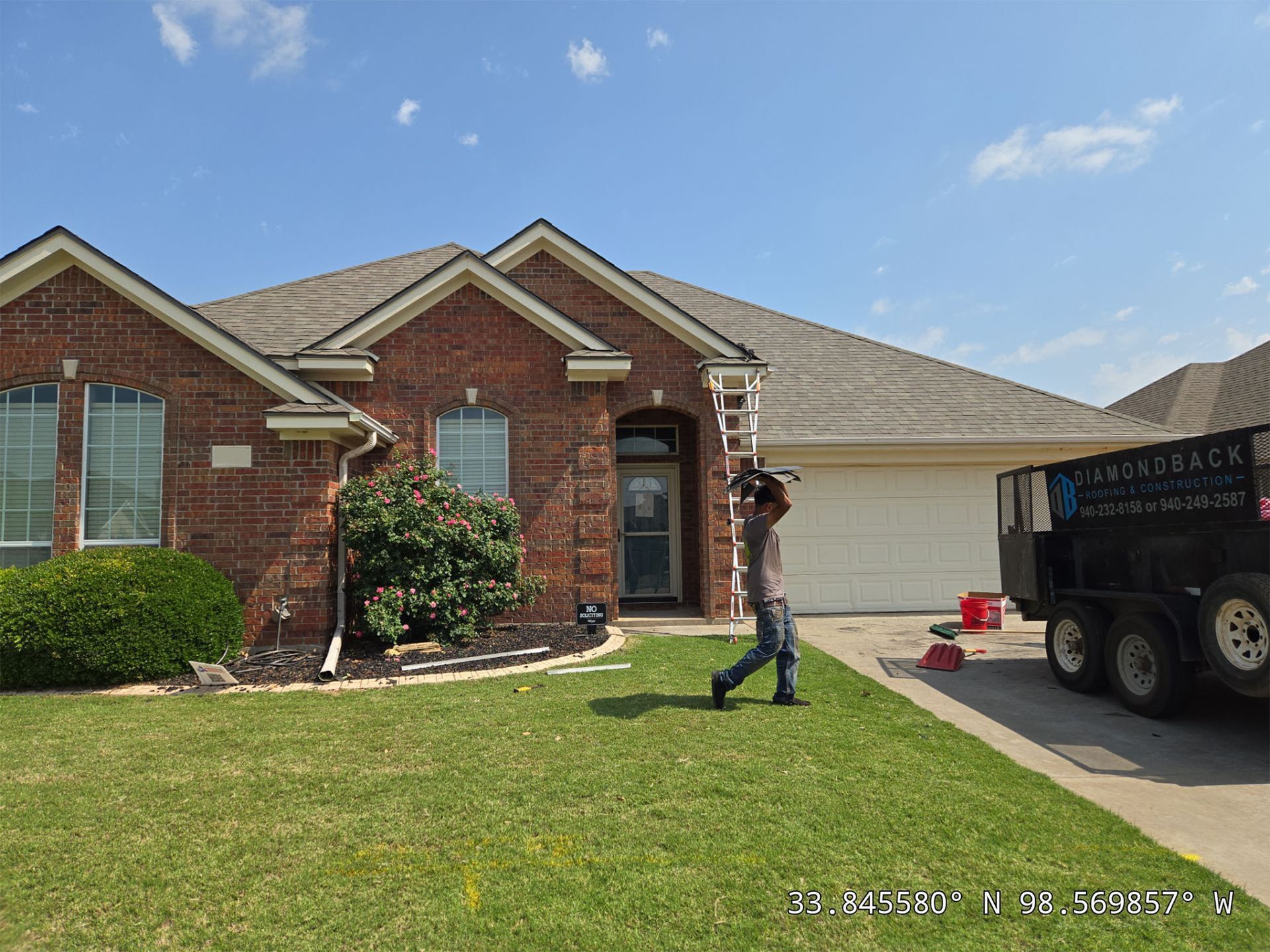 A man is walking in front of a brick house next to a dumpster.