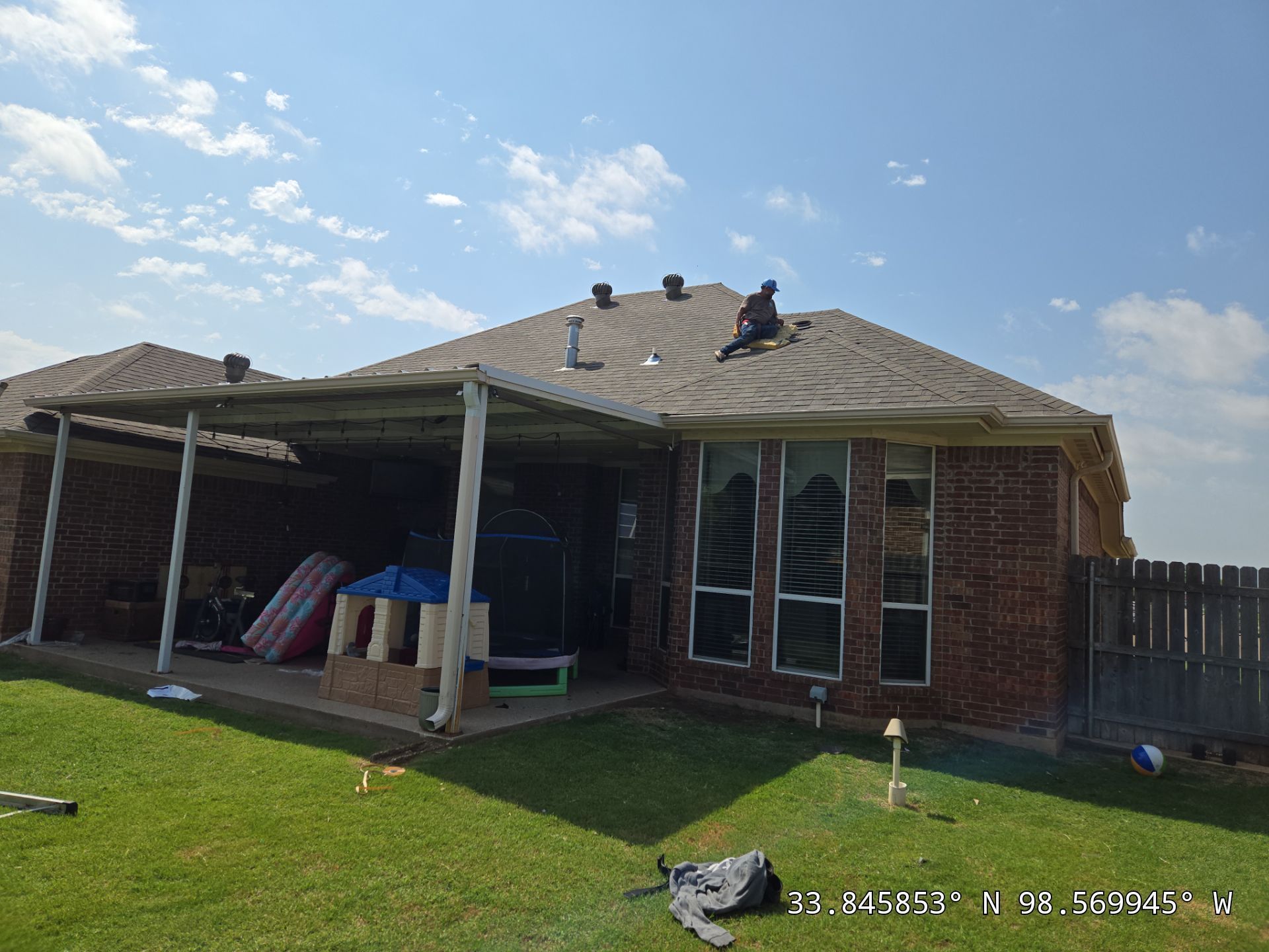 A man is working on the roof of a brick house.
