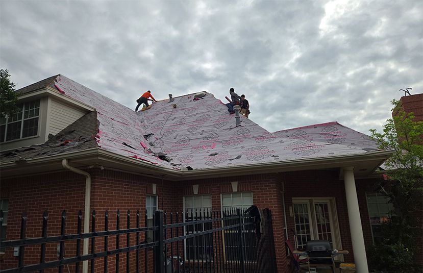 A group of people are working on the roof of a brick house.