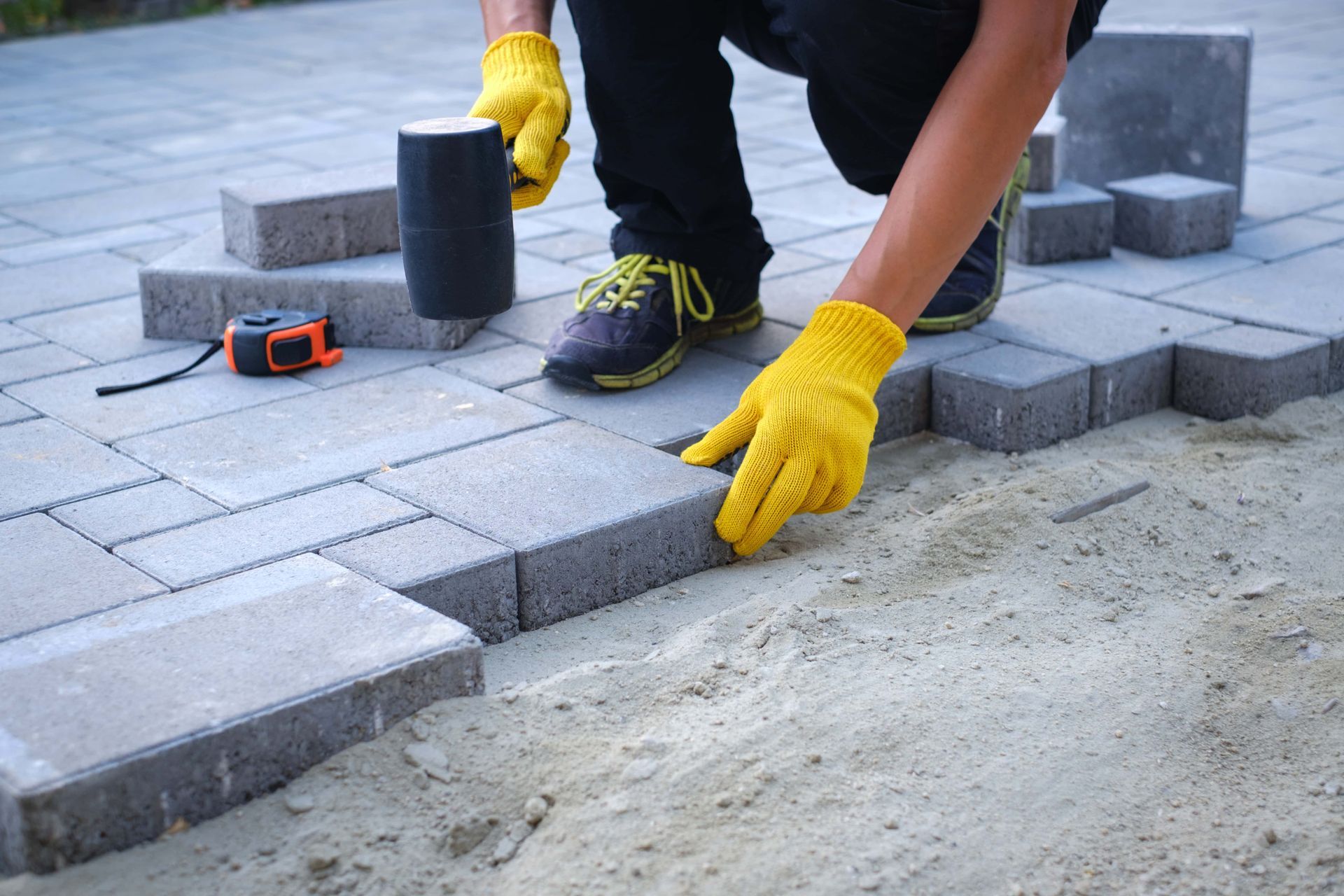 A man wearing yellow gloves is laying bricks on a sidewalk.
