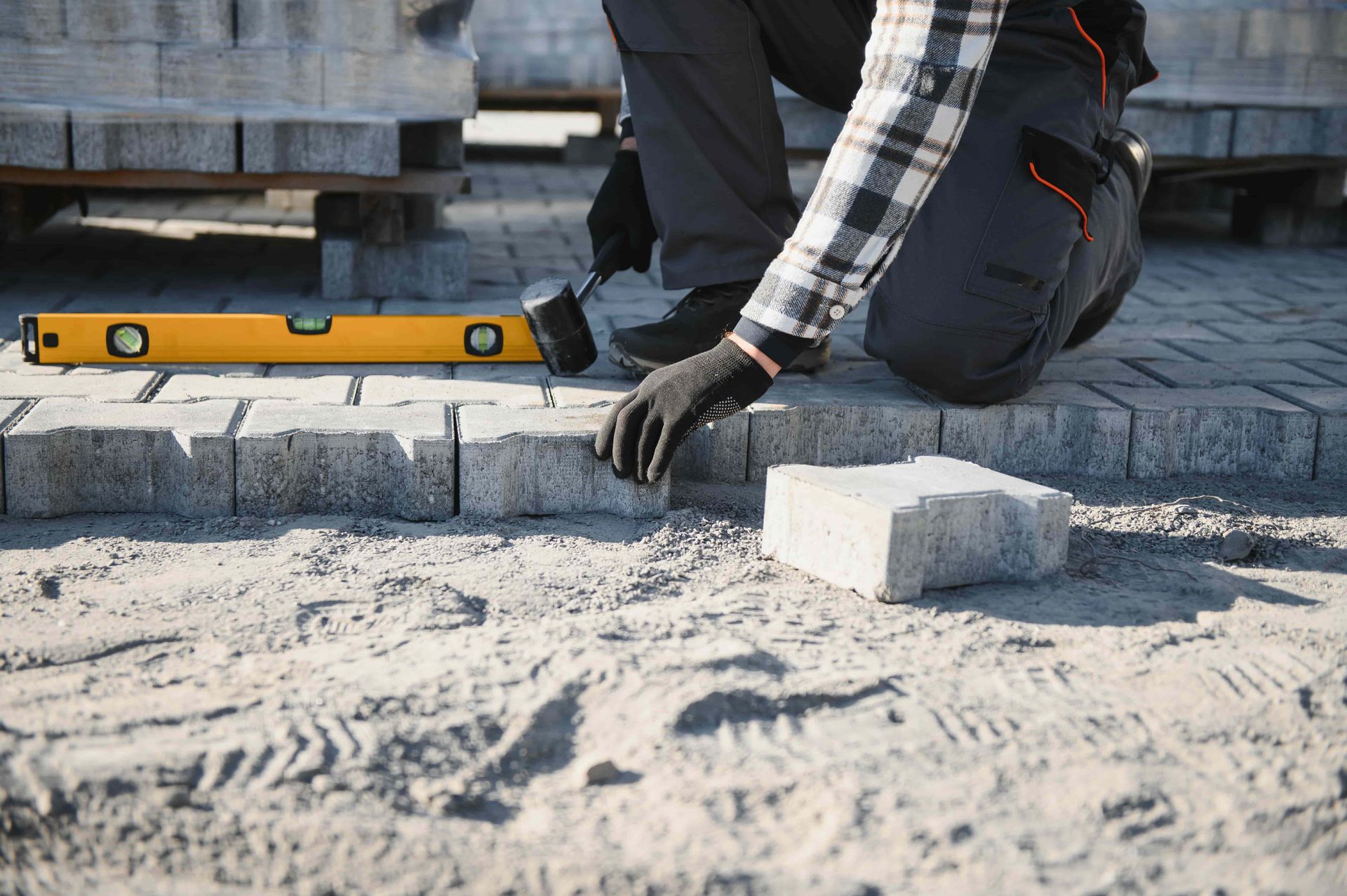 A construction worker is laying bricks on a sidewalk.