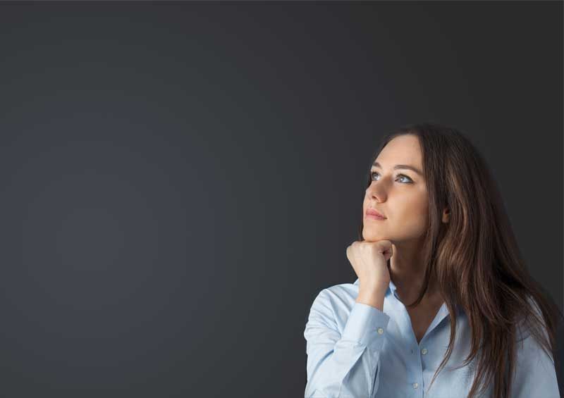 A woman in a blue shirt is looking up with her hand on her chin.