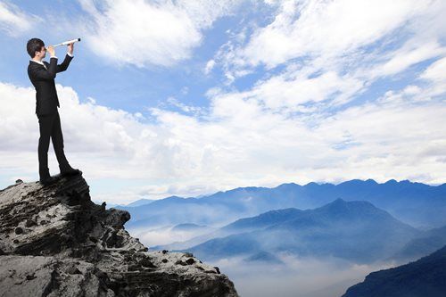 A man is standing on top of a mountain looking through binoculars.