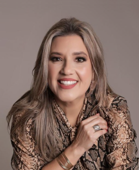 Mulher sorridente com blusa estampada, posando contra um fundo neutro.