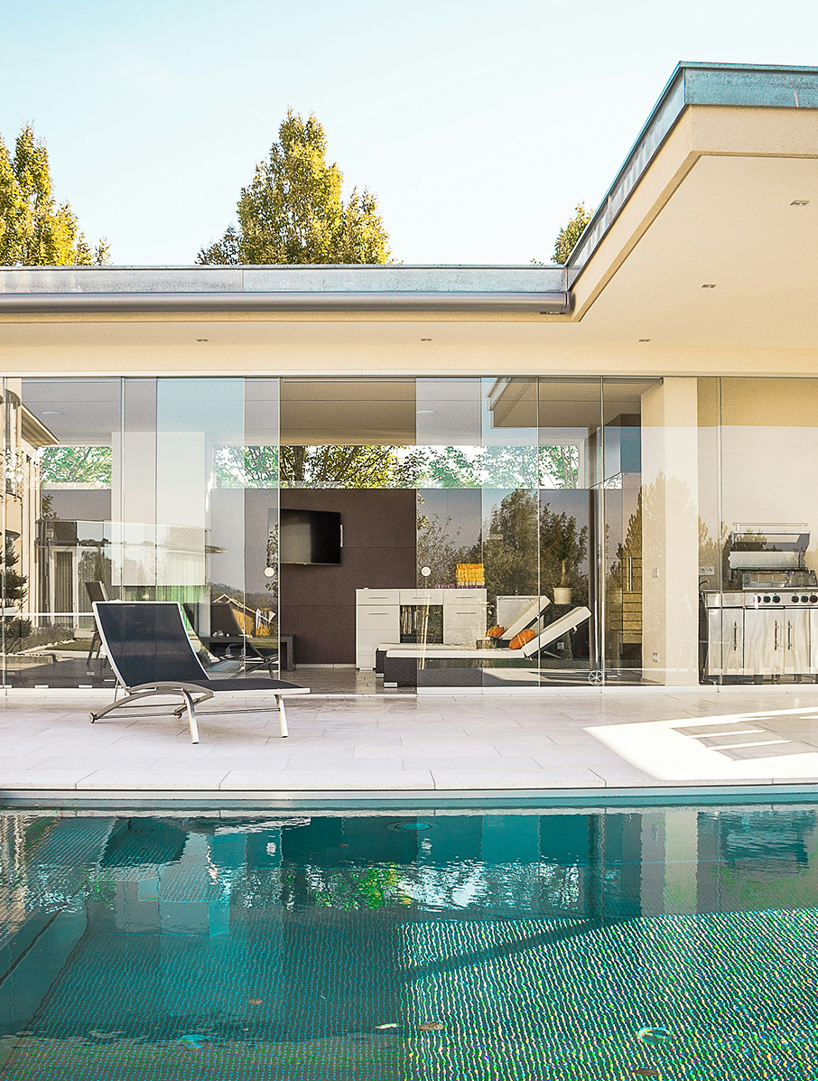 Poolside patio with glass walls, outdoor kitchen, lounge chair, and a pool with turquoise mosaic tiles.