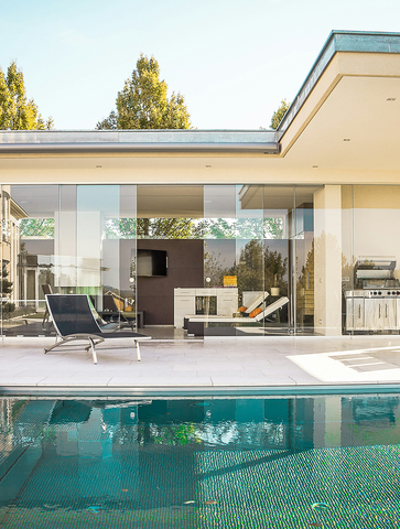 Poolside patio with glass walls, outdoor kitchen, lounge chair, and a pool with turquoise mosaic tiles.