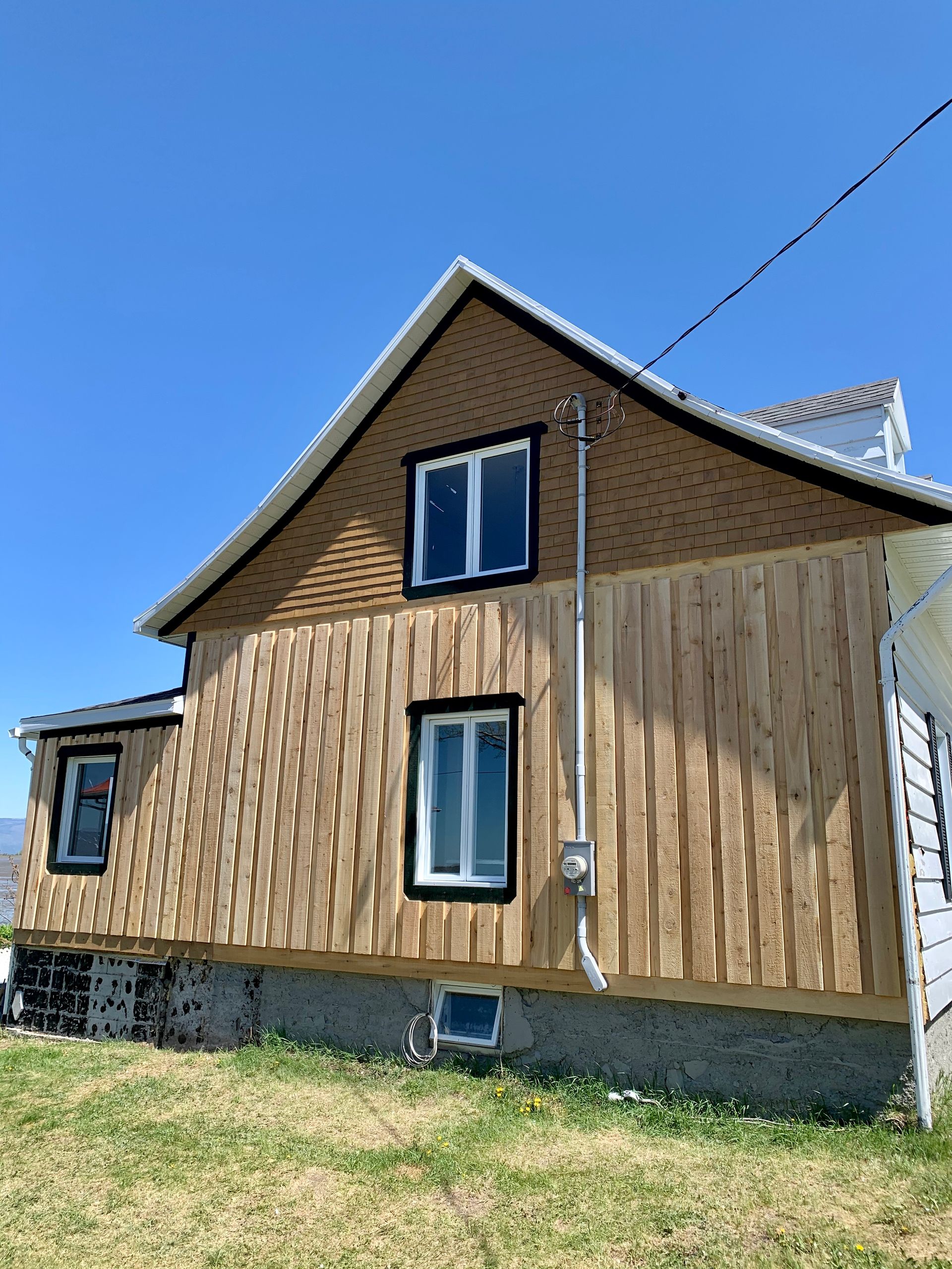 Une maison avec un revêtement en bois et des fenêtres se trouve au milieu d’un champ herbeux.