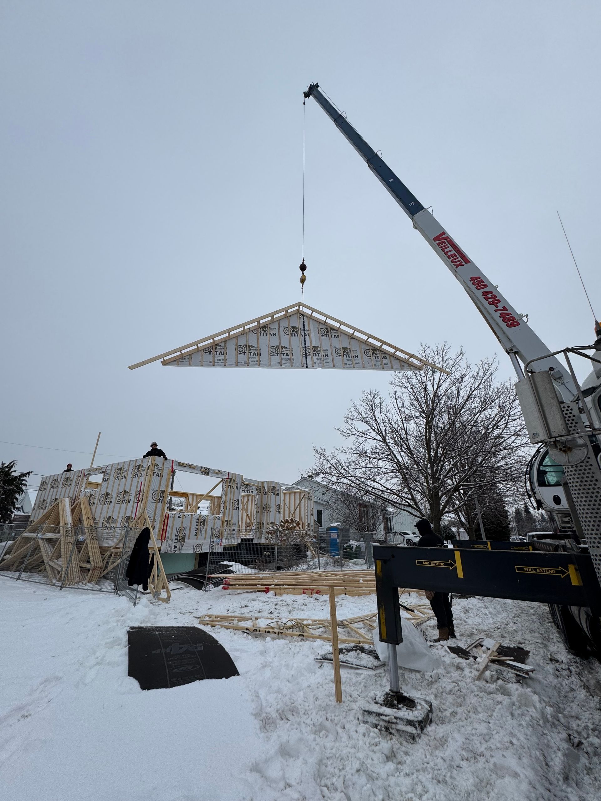 Une grue soulève un toit dans la neige
