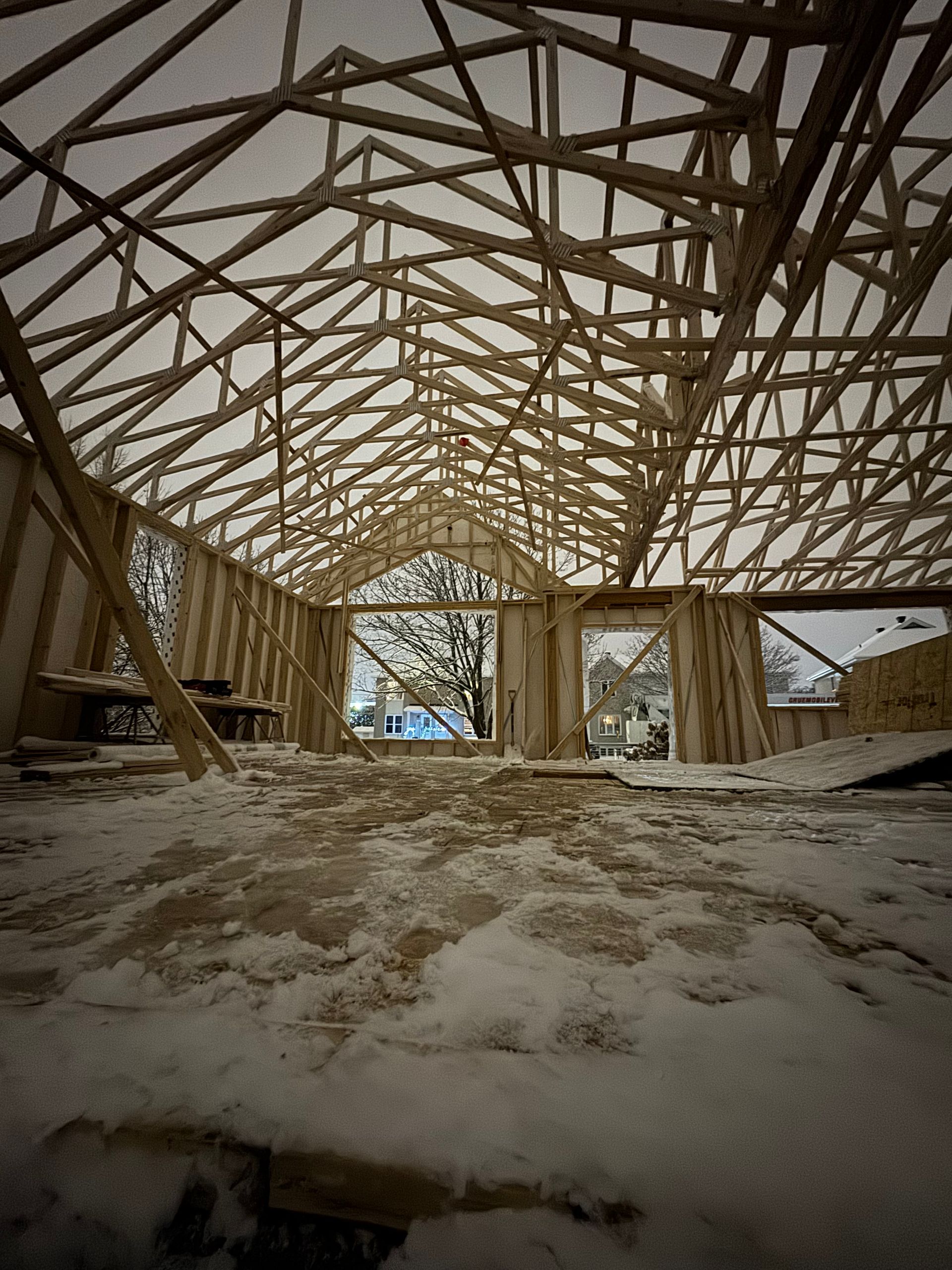 Intérieur enneigé d'une structure en bois en construction, vu de l'intérieur, avec une porte ouverte.