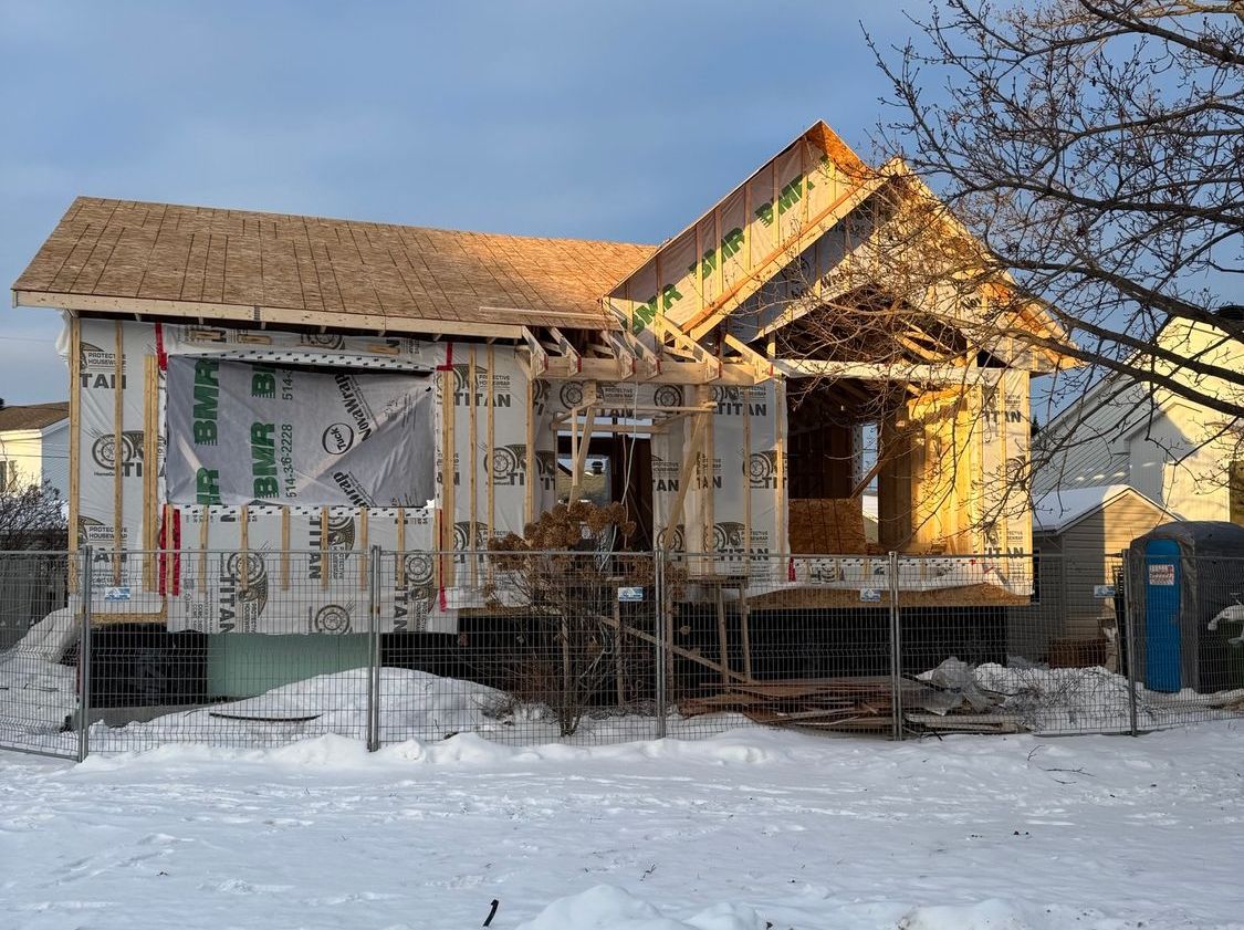 Une maison en construction avec ossature bois apparente, enveloppée de matériaux protecteurs, dans un environnement enneigé.