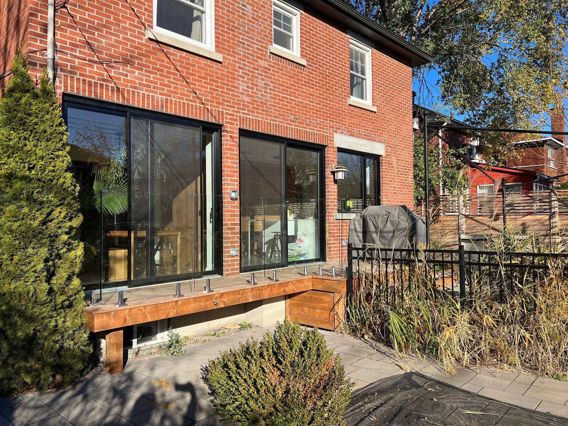 Bâtiment en briques rouges avec de grandes fenêtres à cadre noir et une petite terrasse, face à une cour.