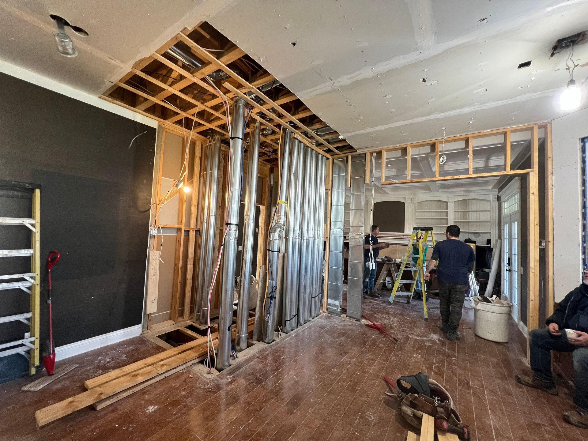 Interior view of a room under renovation, showing exposed framing, ductwork, and people working.