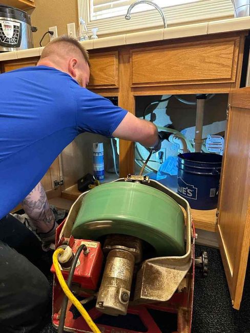 Plumber working under a kitchen sink using a drain cleaning machine.