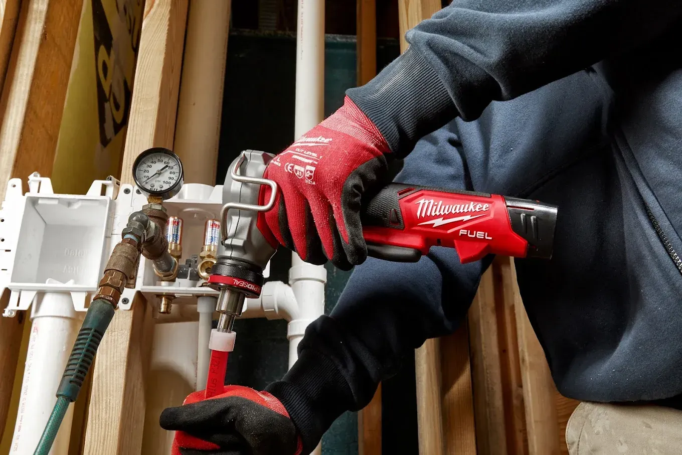 Person using a red Milwaukee tool to work on plumbing pipes, indoors.