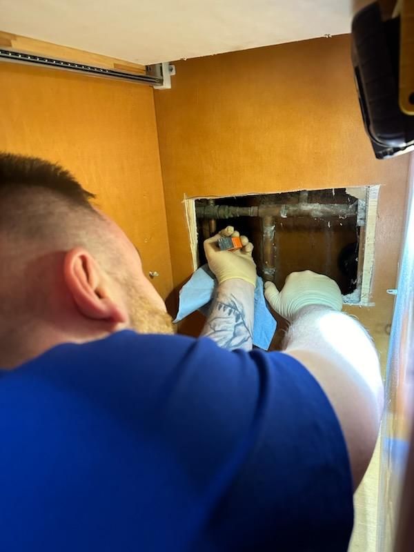 Person working on pipes inside a wall, wearing gloves.