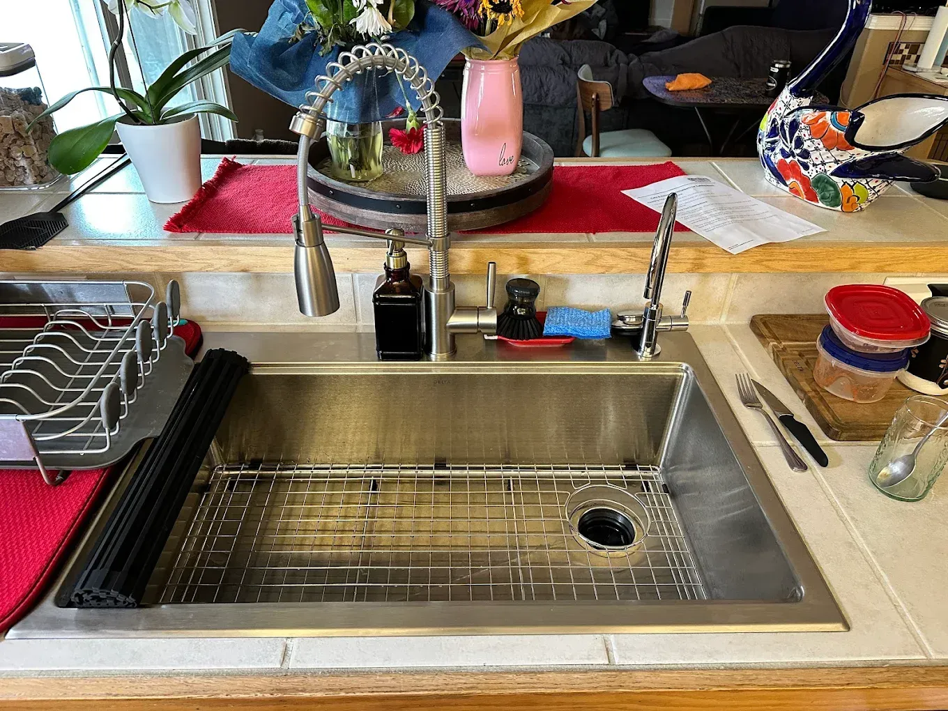 Stainless steel kitchen sink with faucet, drain rack, and various items on the countertop.